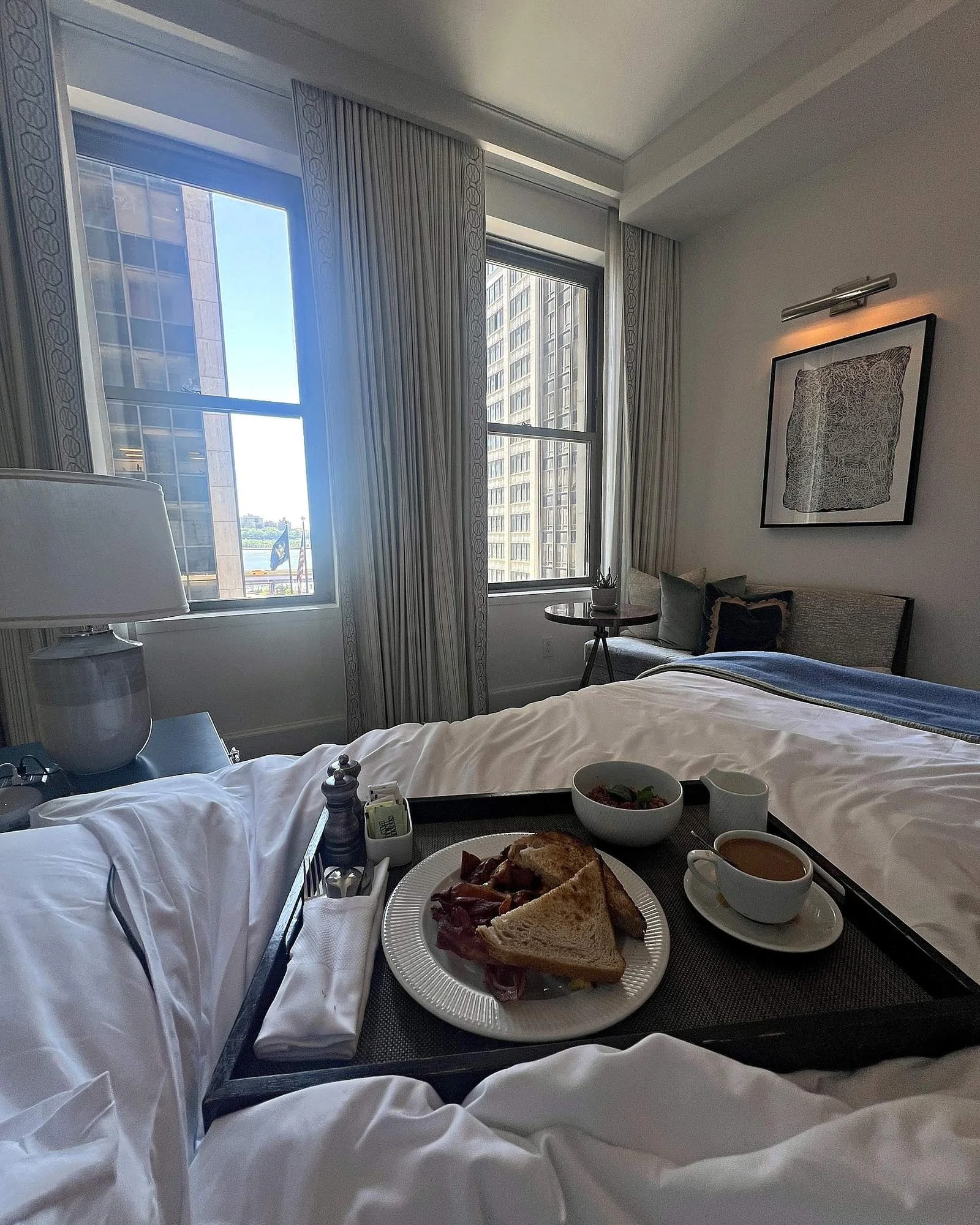 A breakfast tray on the bed at The Wall Street Hotel, windows open to the city.
