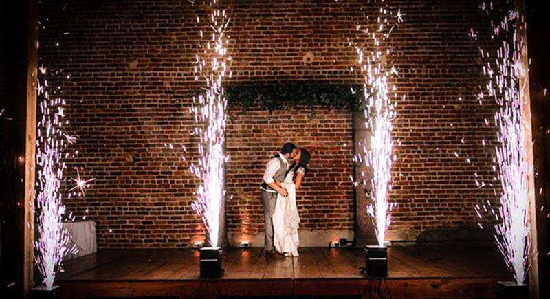 Couple dancing in front of a brick wall with fireworks and sparklers on the floor at a celebration or wedding event.