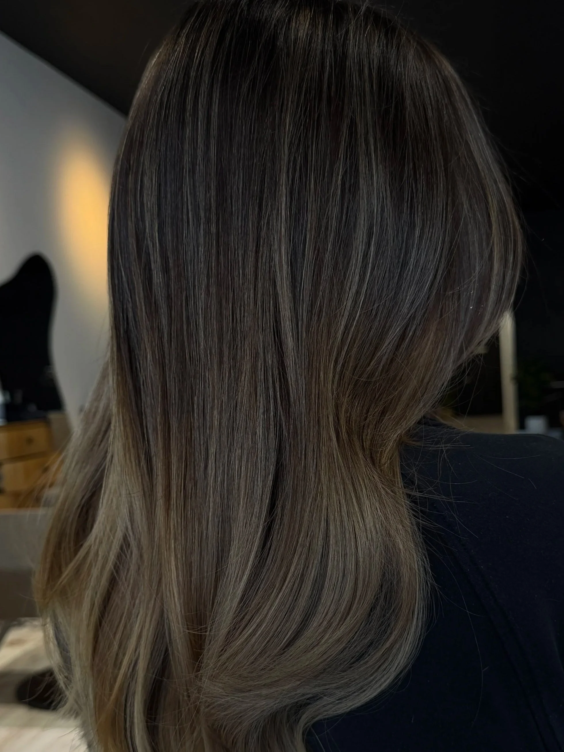 Close-up of a person's hair with a mix of blonde and light brown shades, styled straight with highlights, in a salon setting.