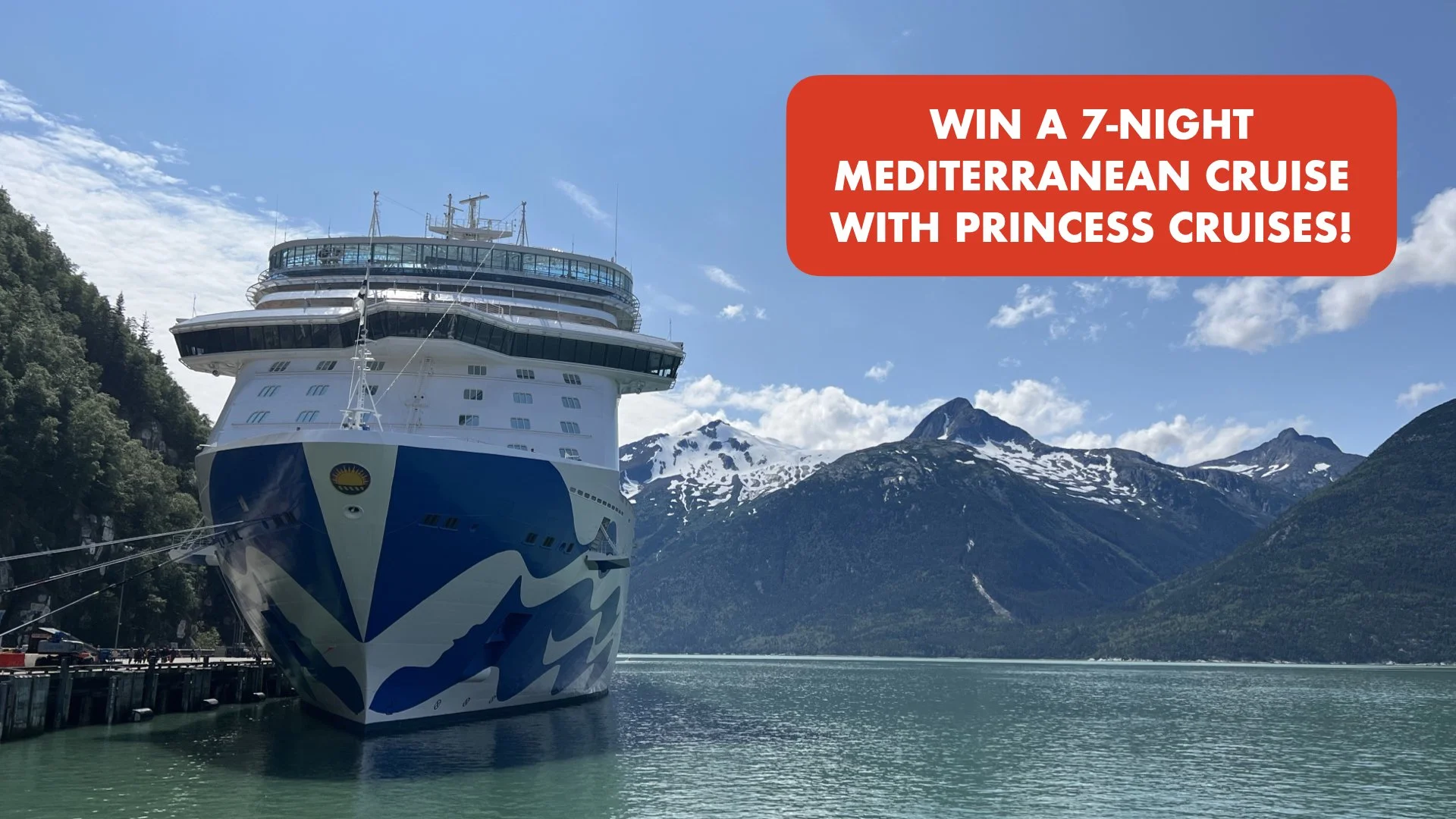 A large cruise ship docked near a mountainous shoreline with snow-capped peaks in the background and a partly cloudy blue sky. A red banner with white text advertises a chance to win a Mediterranean cruise.