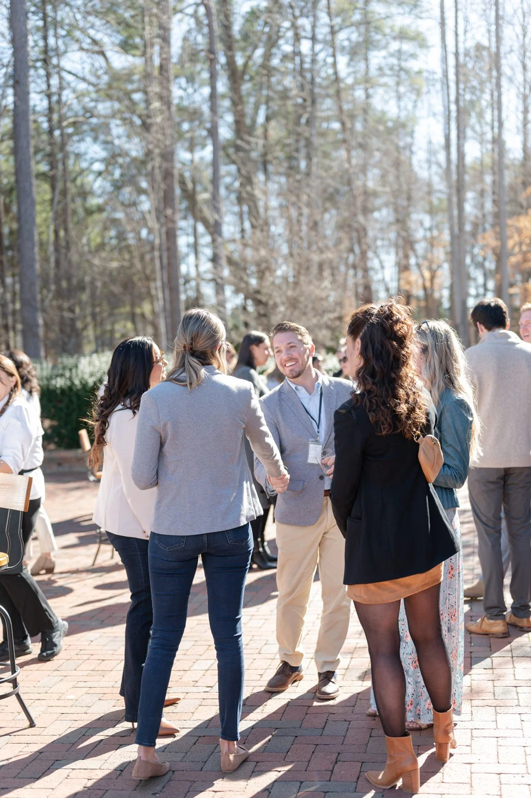 People socializing outdoors in a park-like setting with trees in the background, dressed in business casual attire.