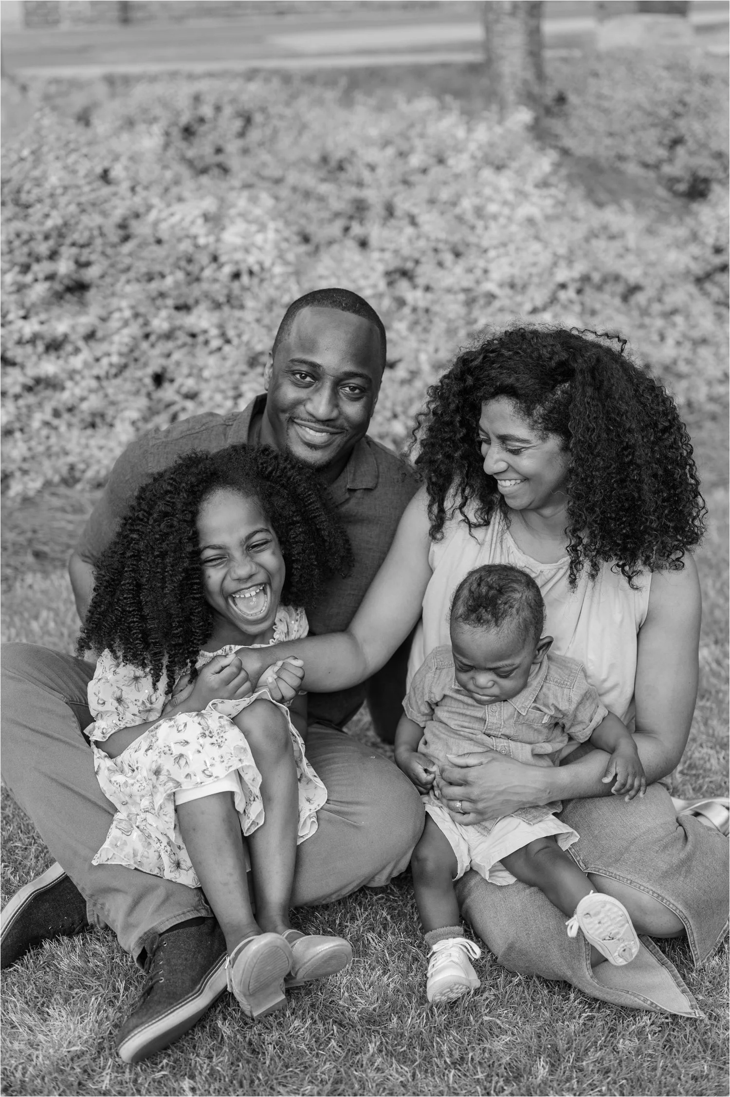 A black family sitting on grass outdoors, enjoying a happy moment together.