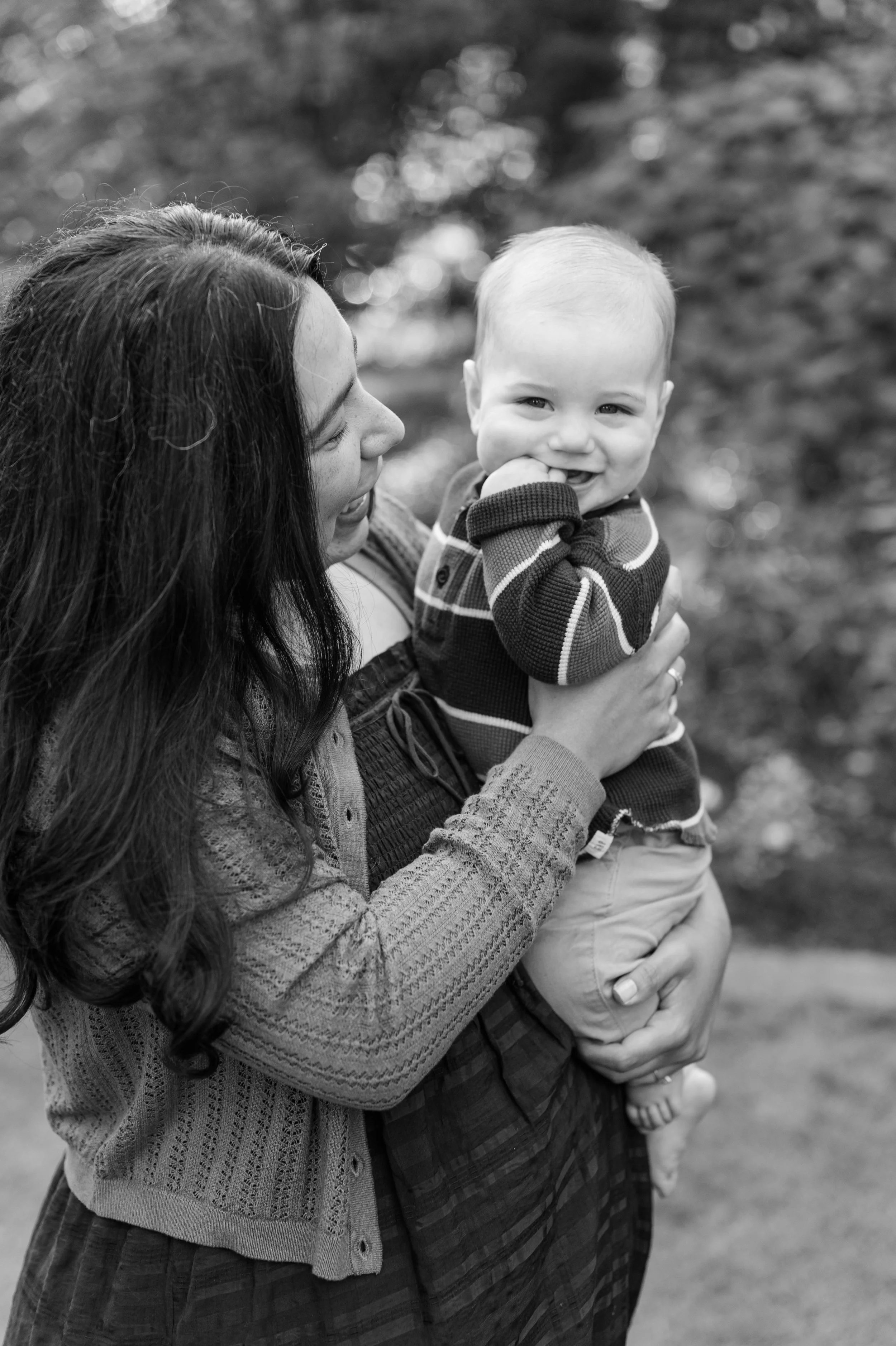 A woman holding a smiling baby boy outside in a natural setting, black and white photograph.