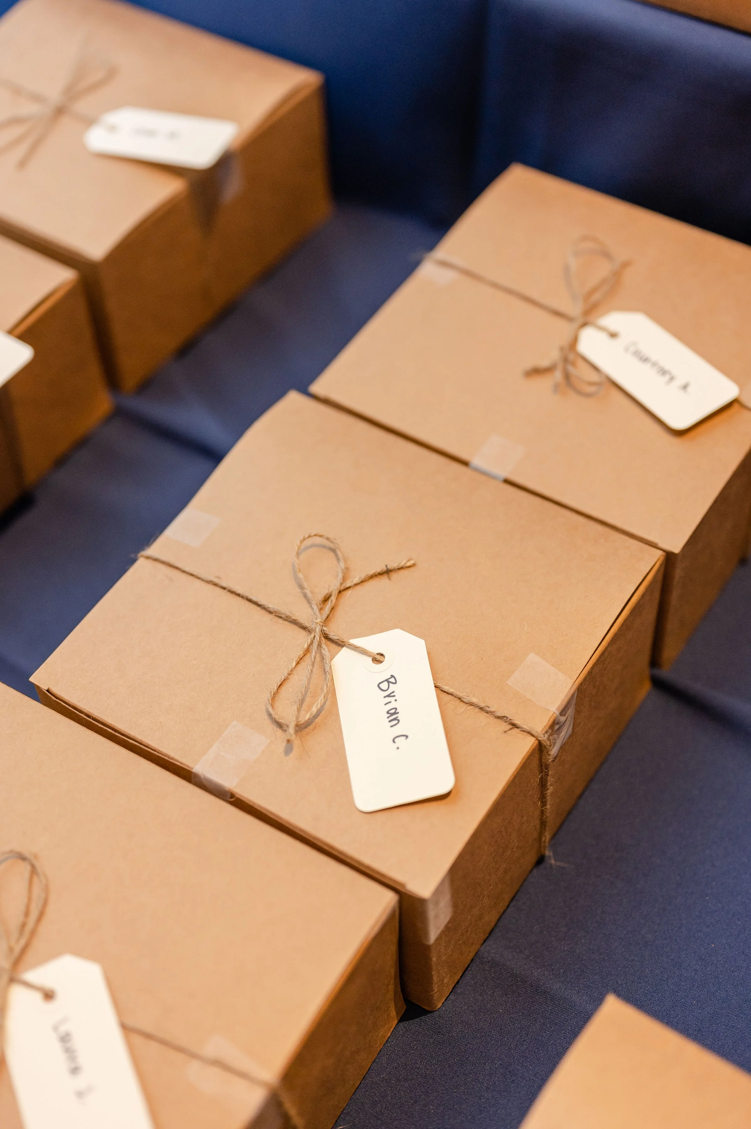Several brown cardboard boxes sealed with string and labeled with white tags, placed on a dark blue surface.