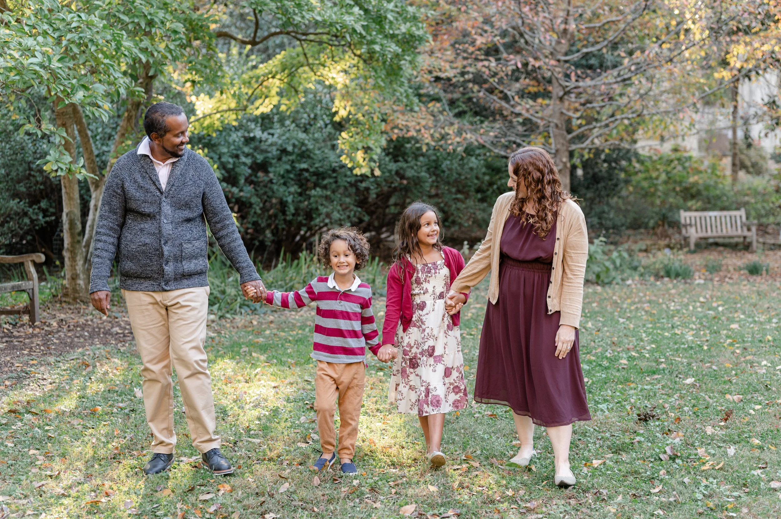 A family of five walking hand in hand in a park during autumn.