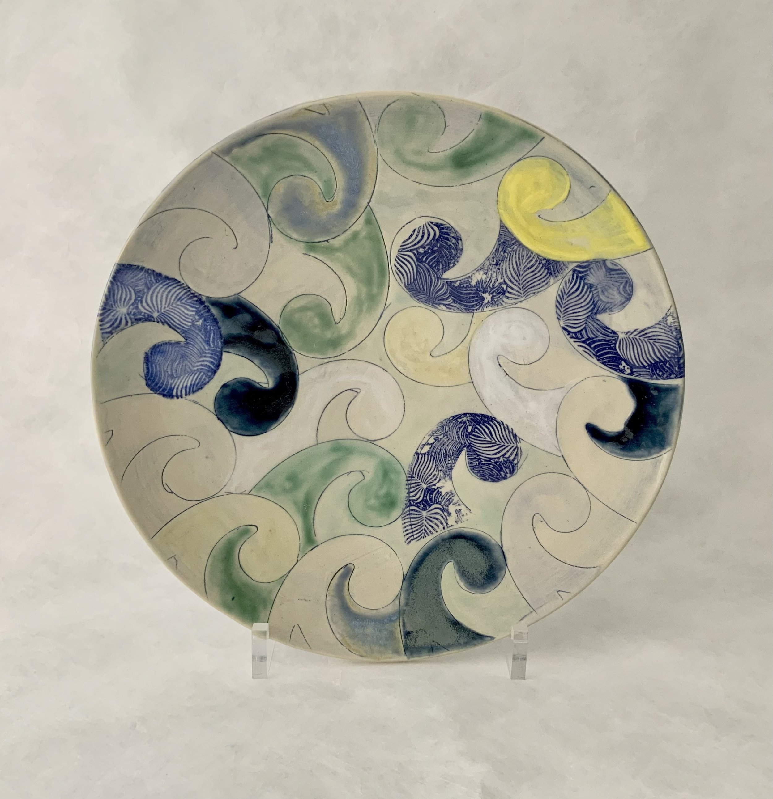 Ceramic plate with a swirling wave pattern in blue, green, yellow, and white colors.
