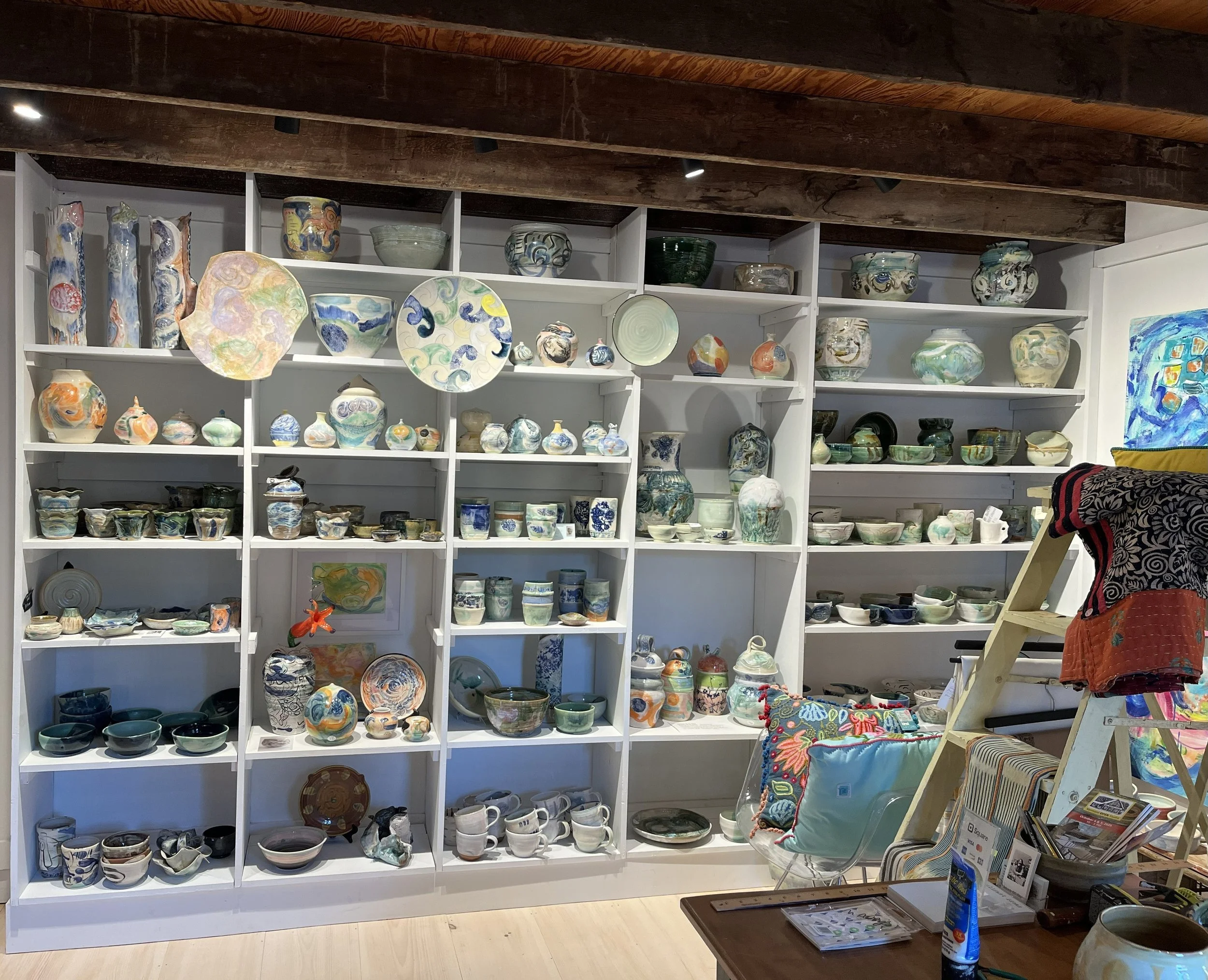 Shelves filled with various hand-painted ceramic bowls, vases, and plates in a store or gallery setting.