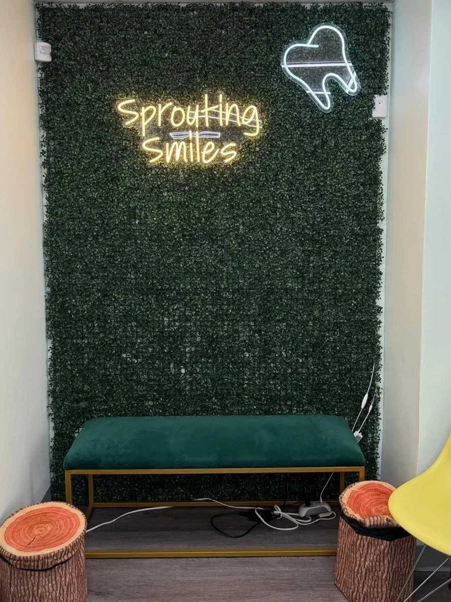 to the right of entrance: green plant wall with neon tooth and "sprouting smiles" signs with emrald green bench and wooden log storage on either side on floor