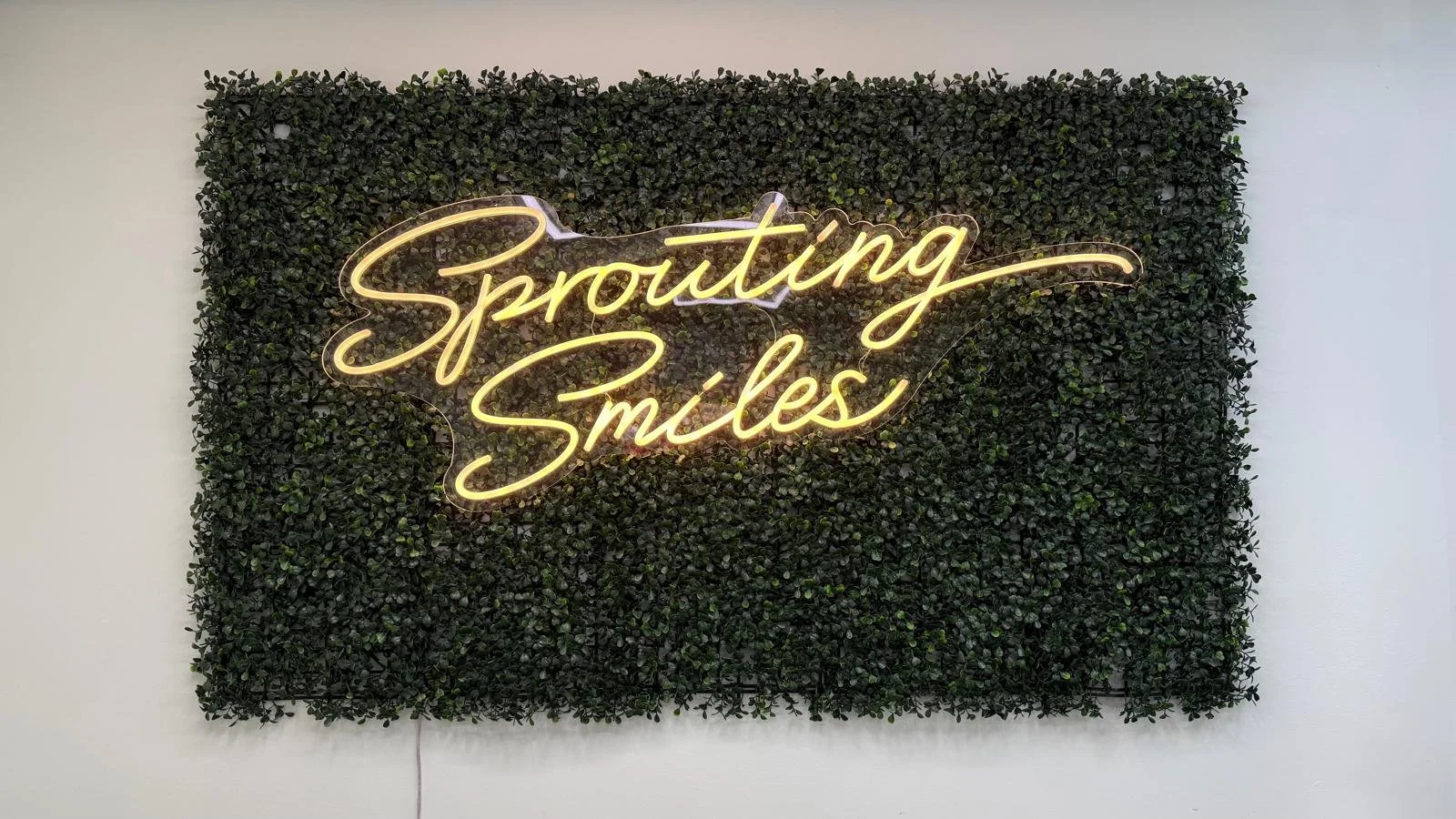 Green plant wall with neon sign that says "sprouting smiles" (located on wall behind reception which is not seen in image)
