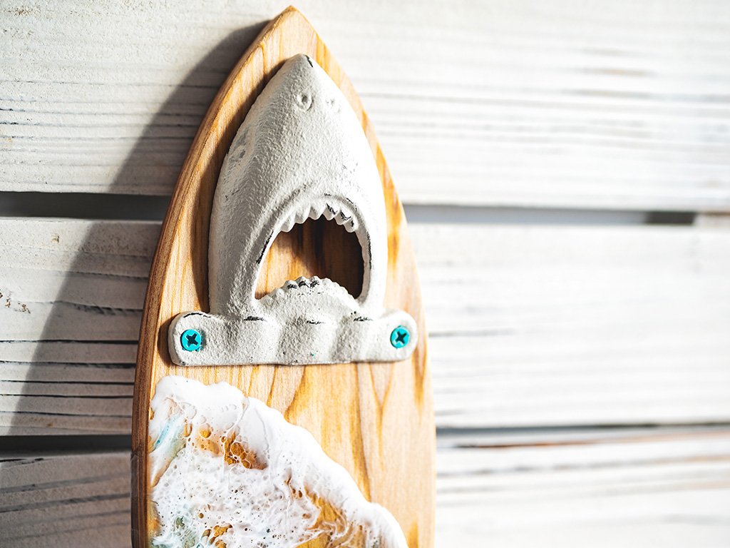 Handcrafted surfboard bottle opener with shark bite and beach waves design.