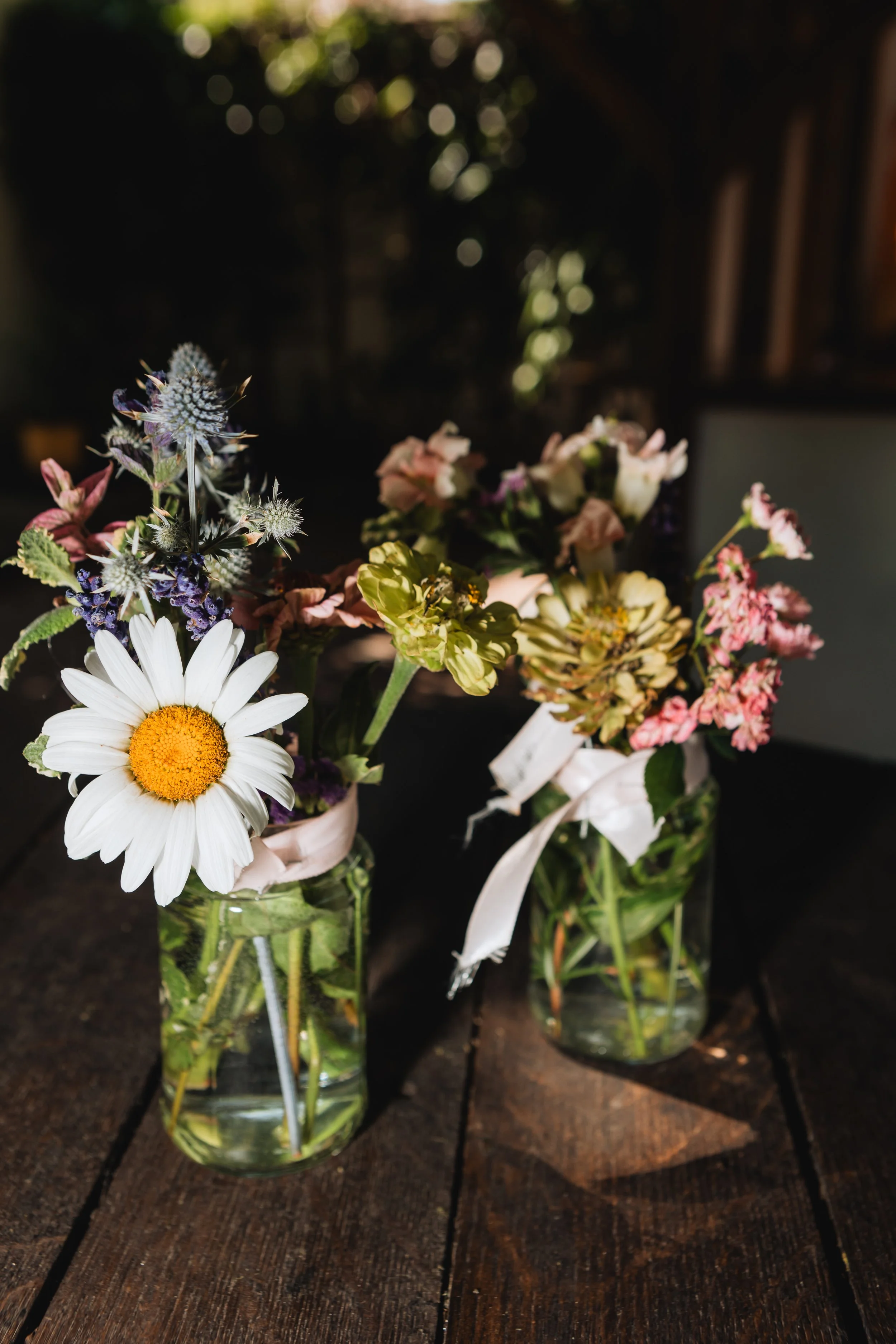 Three mason jars filled with various colorful wildflowers and greenery, placed on a wooden surface.