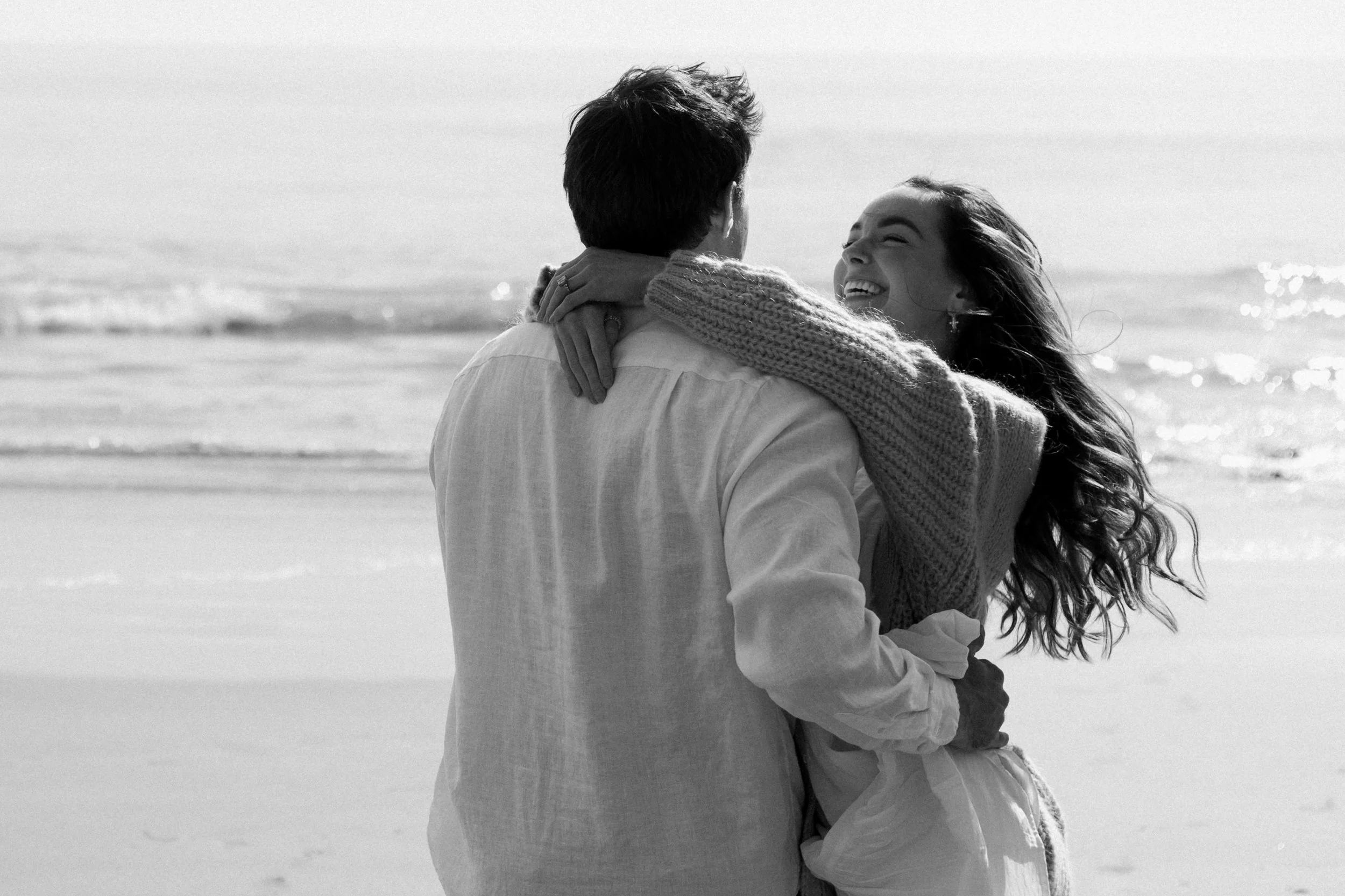A couple embracing on the beach with the ocean in the background, black and white photograph.