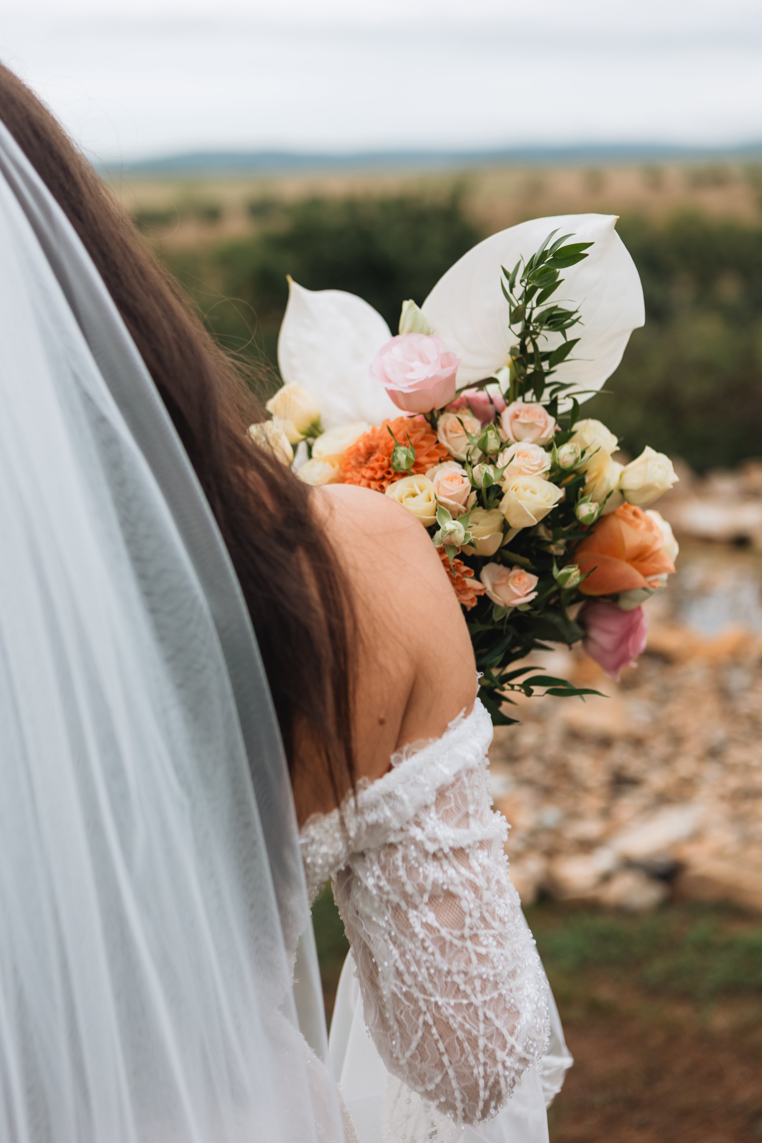 Close-up of a bride holding a bouquet of flowers, with a blurred landscape background.