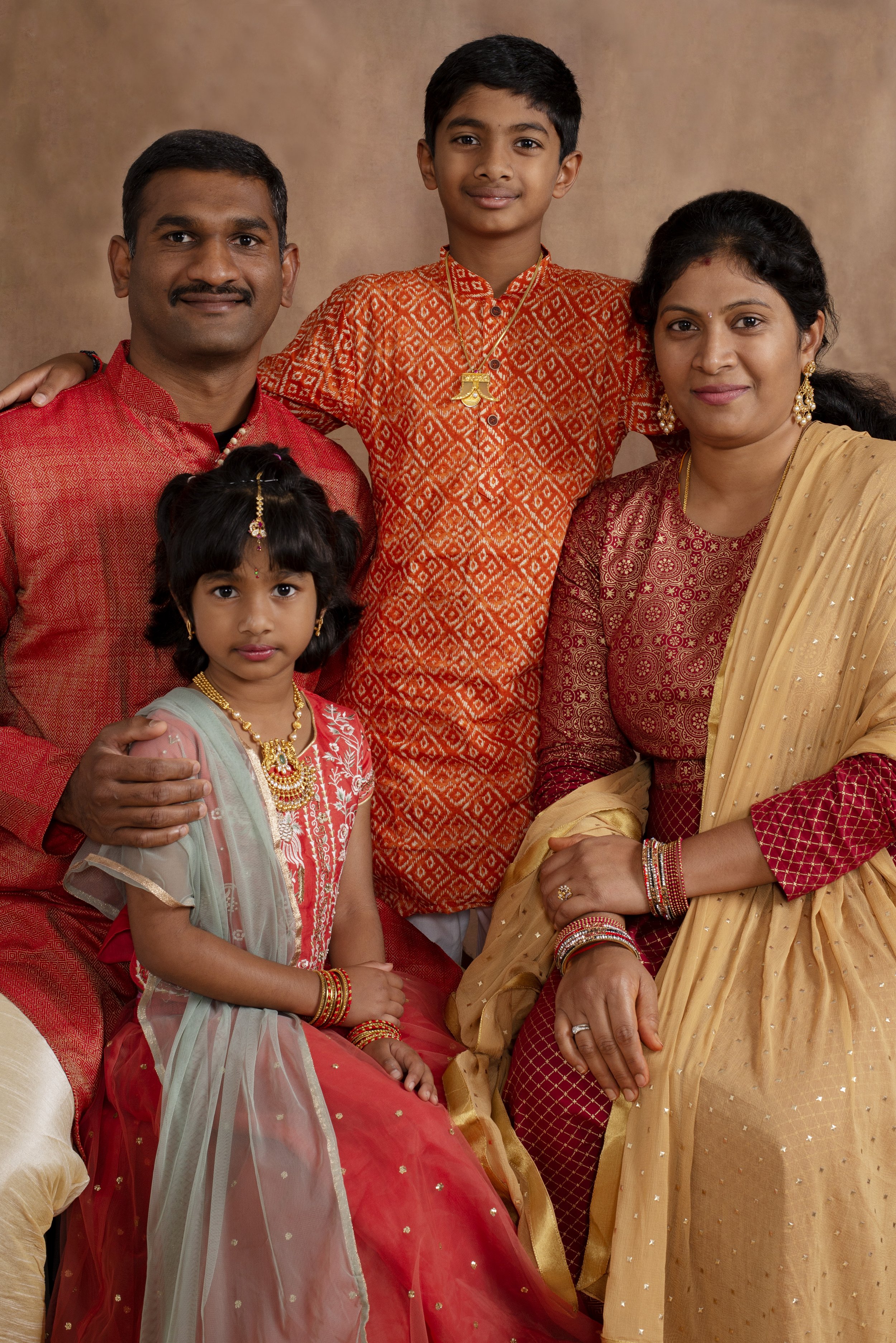 A family portrait featuring five members dressed in traditional Indian attire, posing against a neutral background.