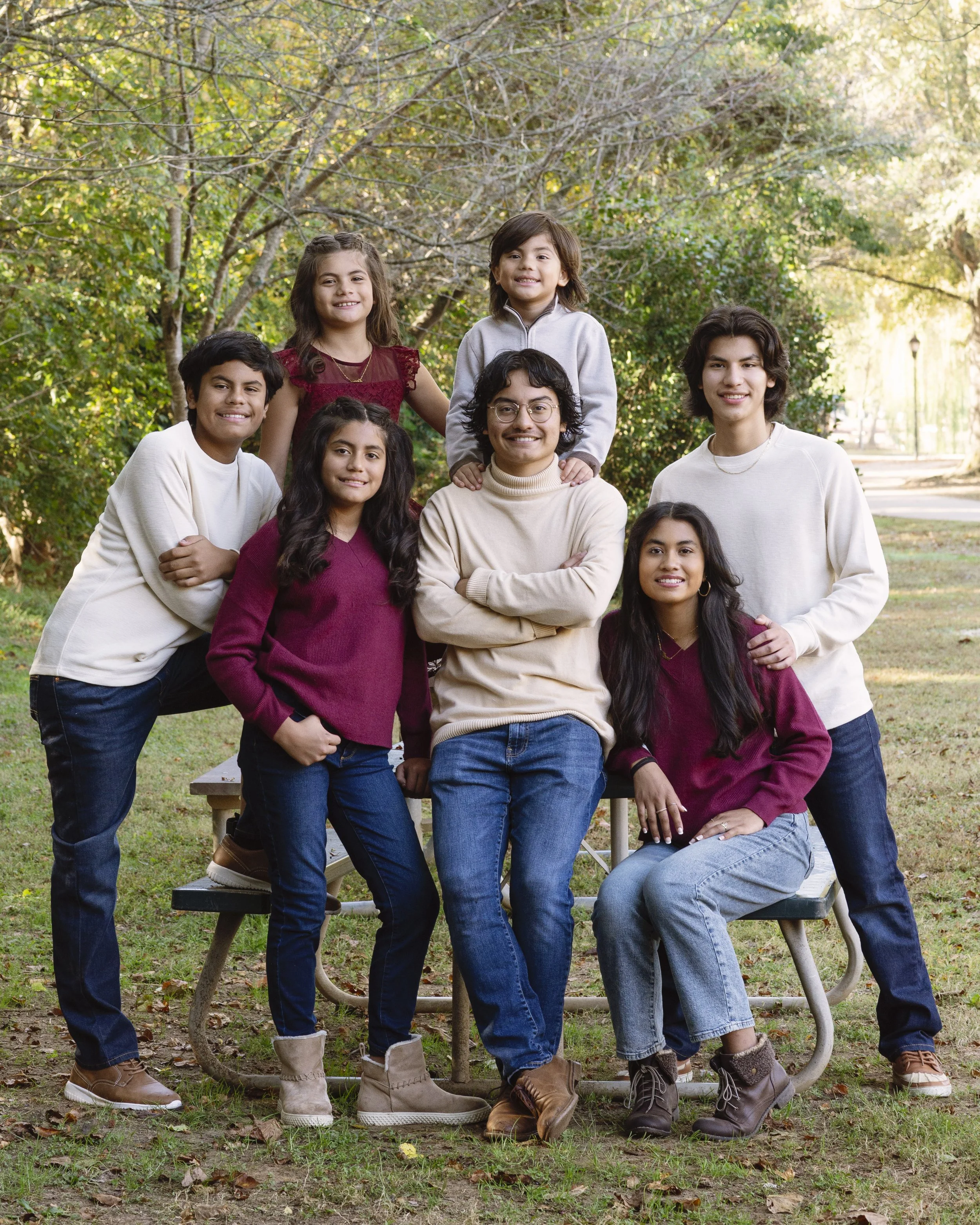 Group of eight diverse children outdoors in a park, posing for a photo with trees and sunlight in the background.