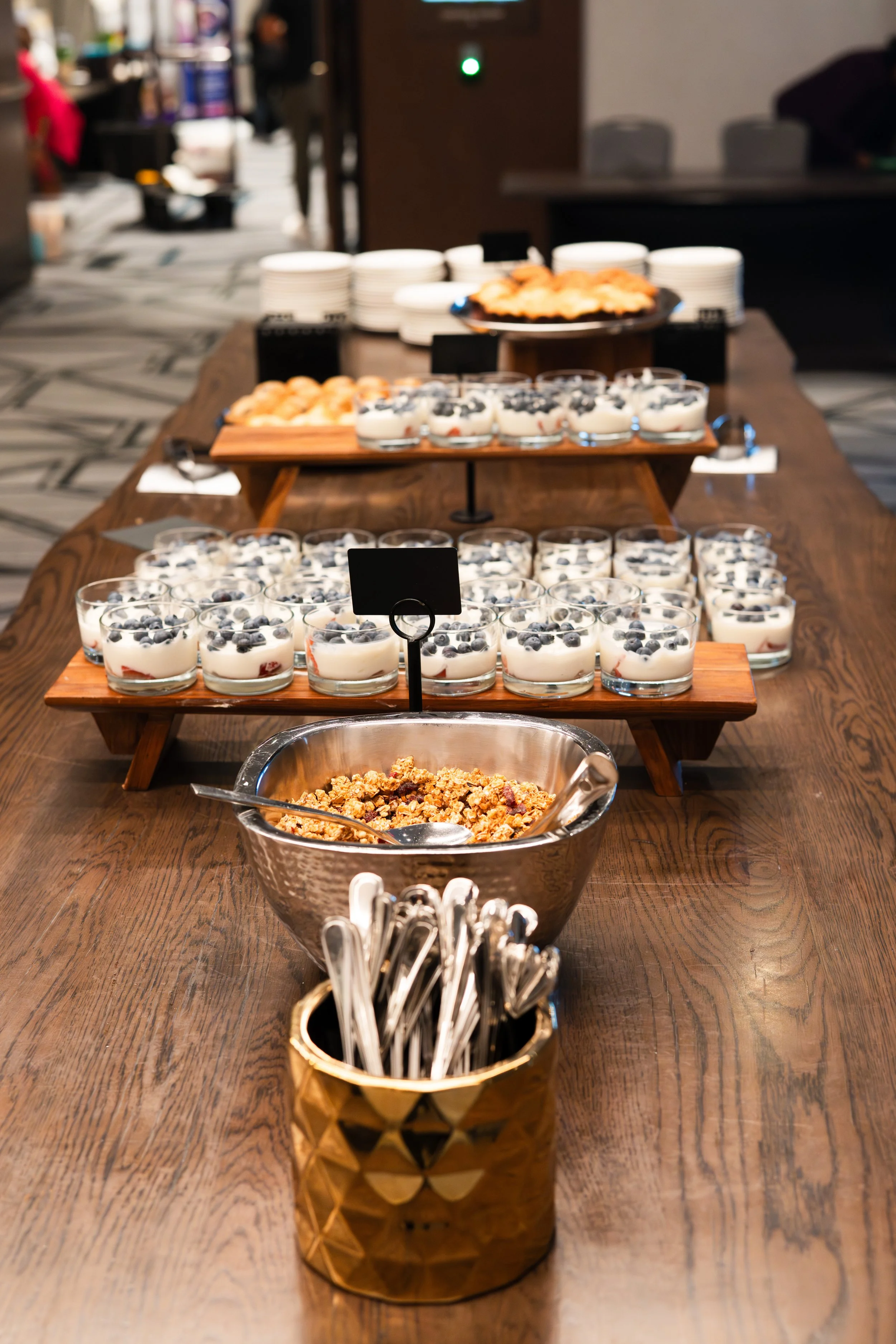 A dessert buffet table with bowls of yogurt topped with blueberries and strawberries, granola, and a variety of other sweet treats in the background.