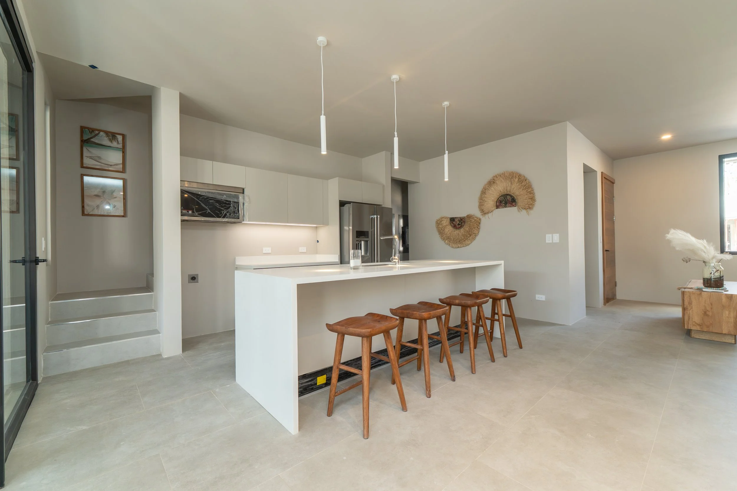Modern kitchen with white island, stainless steel appliances, and wooden bar stools, decorated with wall art and a decorative fan on the wall, in a home with neutral colors and natural light.