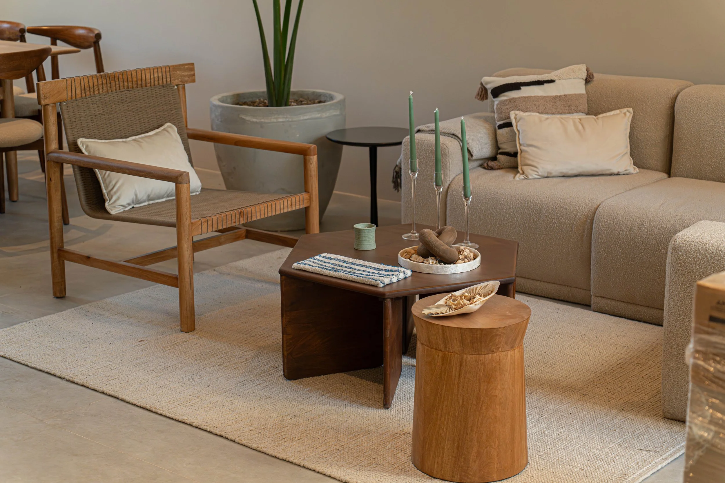 Living room with beige sofa, wooden chairs, a black side table, a large potted plant, and candles on a wooden coffee table.