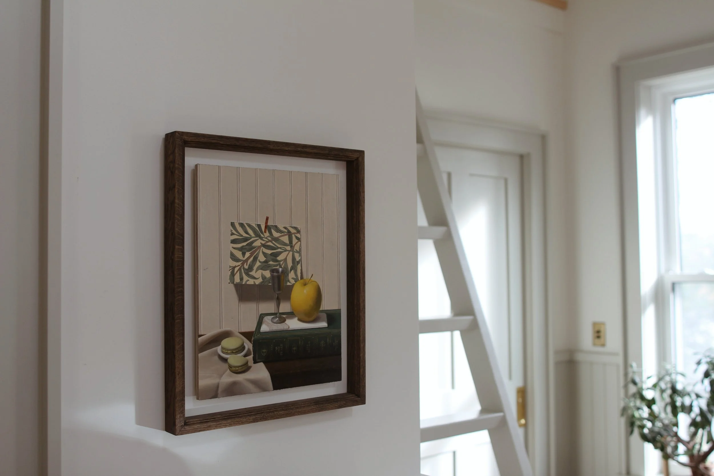 Steep Hill Heirloom Sleeping Cabin interior featuring a still life oil painting in an oak frame on the centre wall in the foreground with a ladder to loft space, a closed pocket door and a tall window with a jade plant in the background.