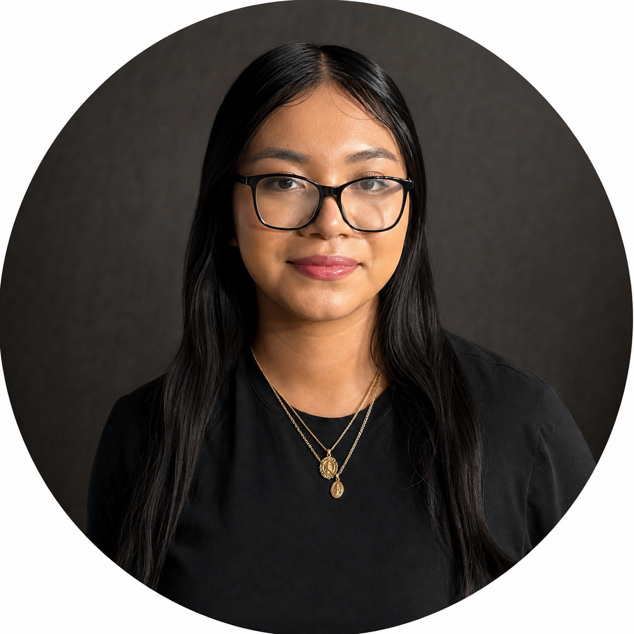 Smiling woman with glasses, black hair with caramel tips, wearing a black jacket and jewelry, standing in front of a wall with colorful letters spelling "STUDENT CENTER".