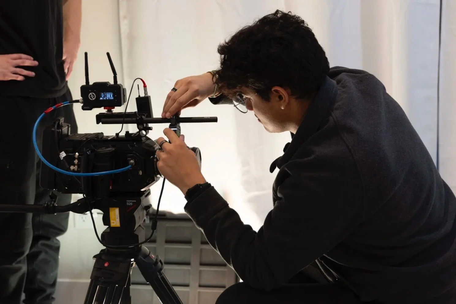 Crew crouched down and adjusting camera equipment on a tripod, in a studio setting, while crew stands nearby.
