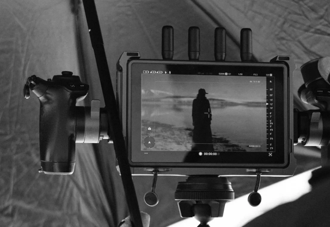 Behind-the-scenes shot of a professional video camera and monitor on the set of GREY, with the monitor displaying a silhouette of a Regina Simons standing outdoors.
