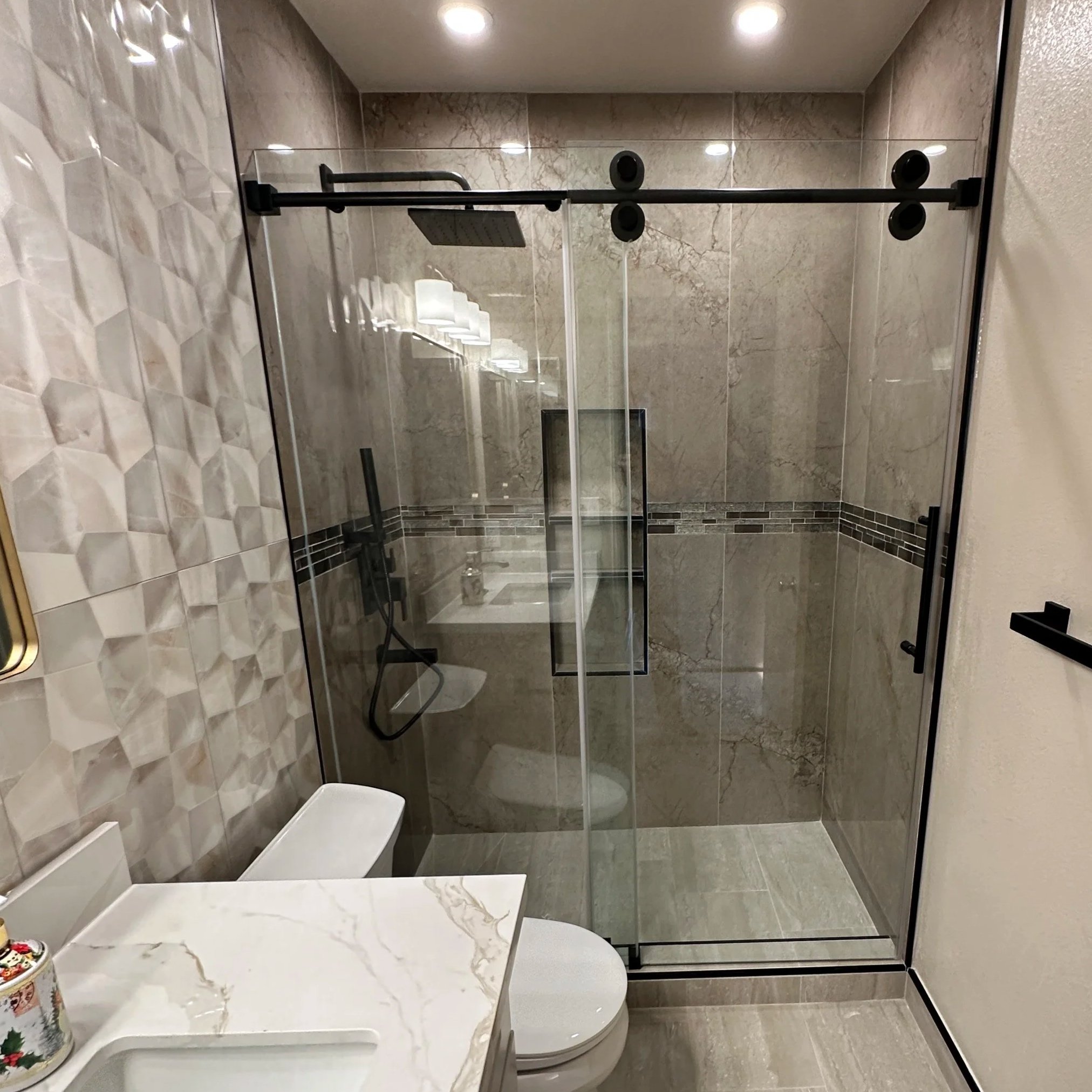 Modern bathroom with a glass shower enclosure, marble countertop sink, and beige tiled floor.