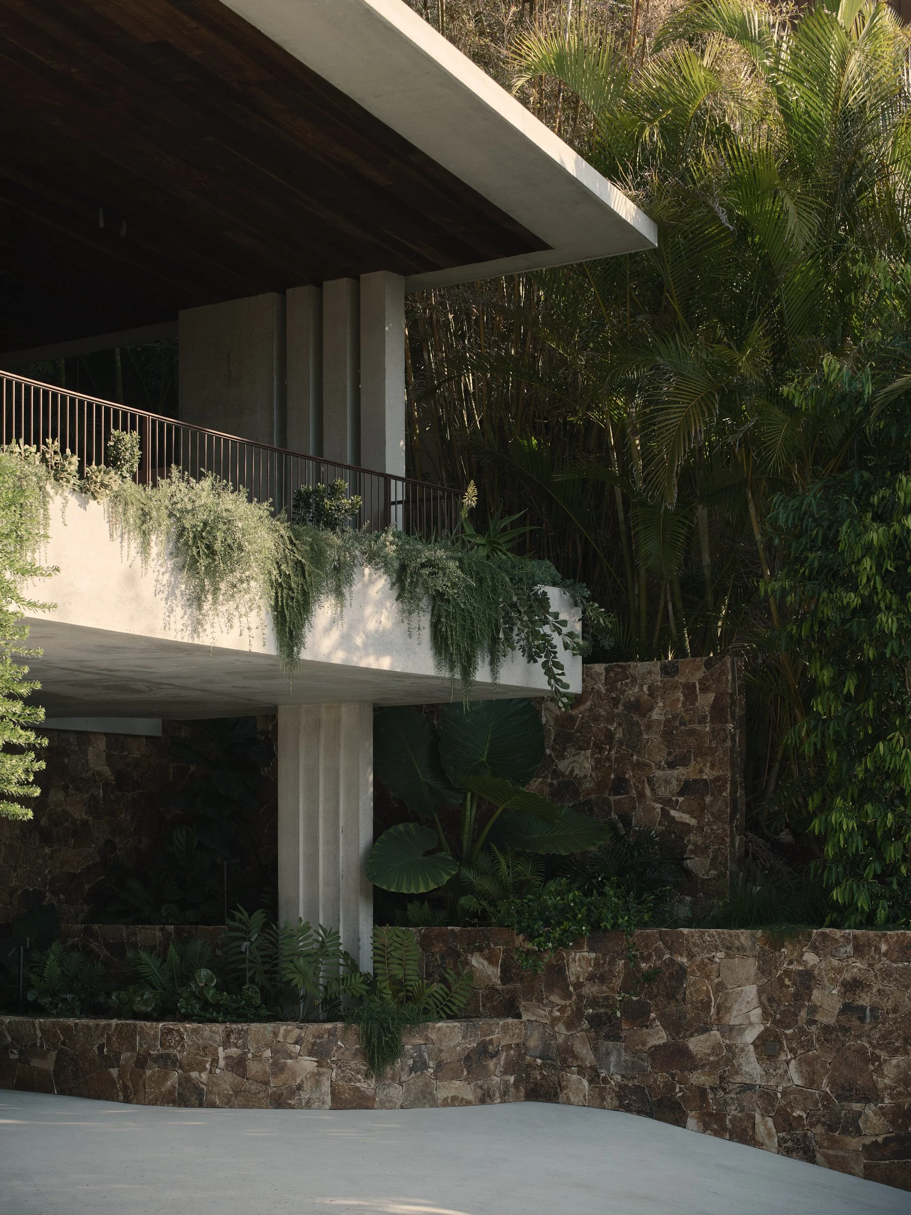 Modern house with outdoor patio, surrounded by lush greenery, stone wall, and plants.