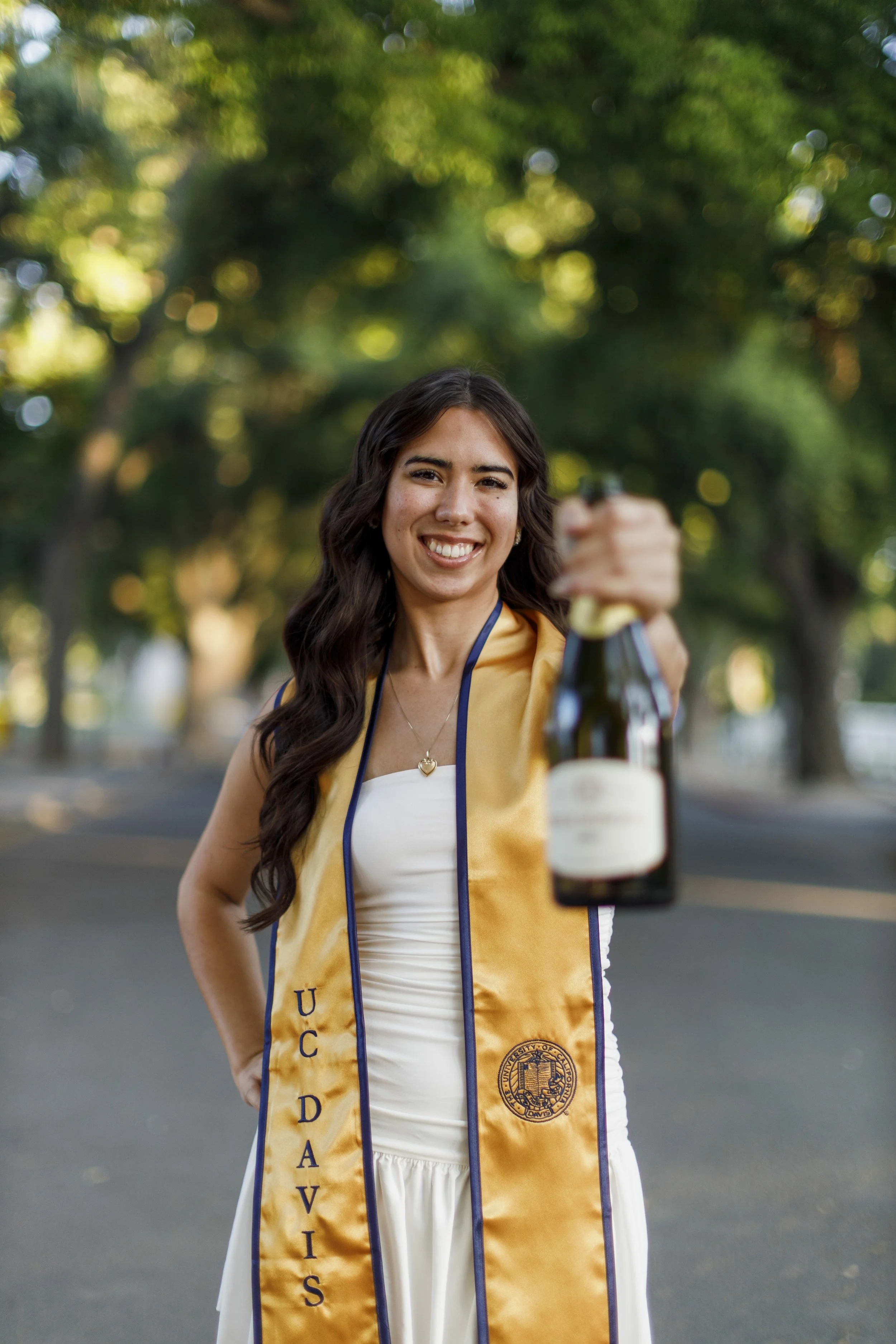 UC Davis graduate smiling and cheers-ing the camera with her bottle of champagne.