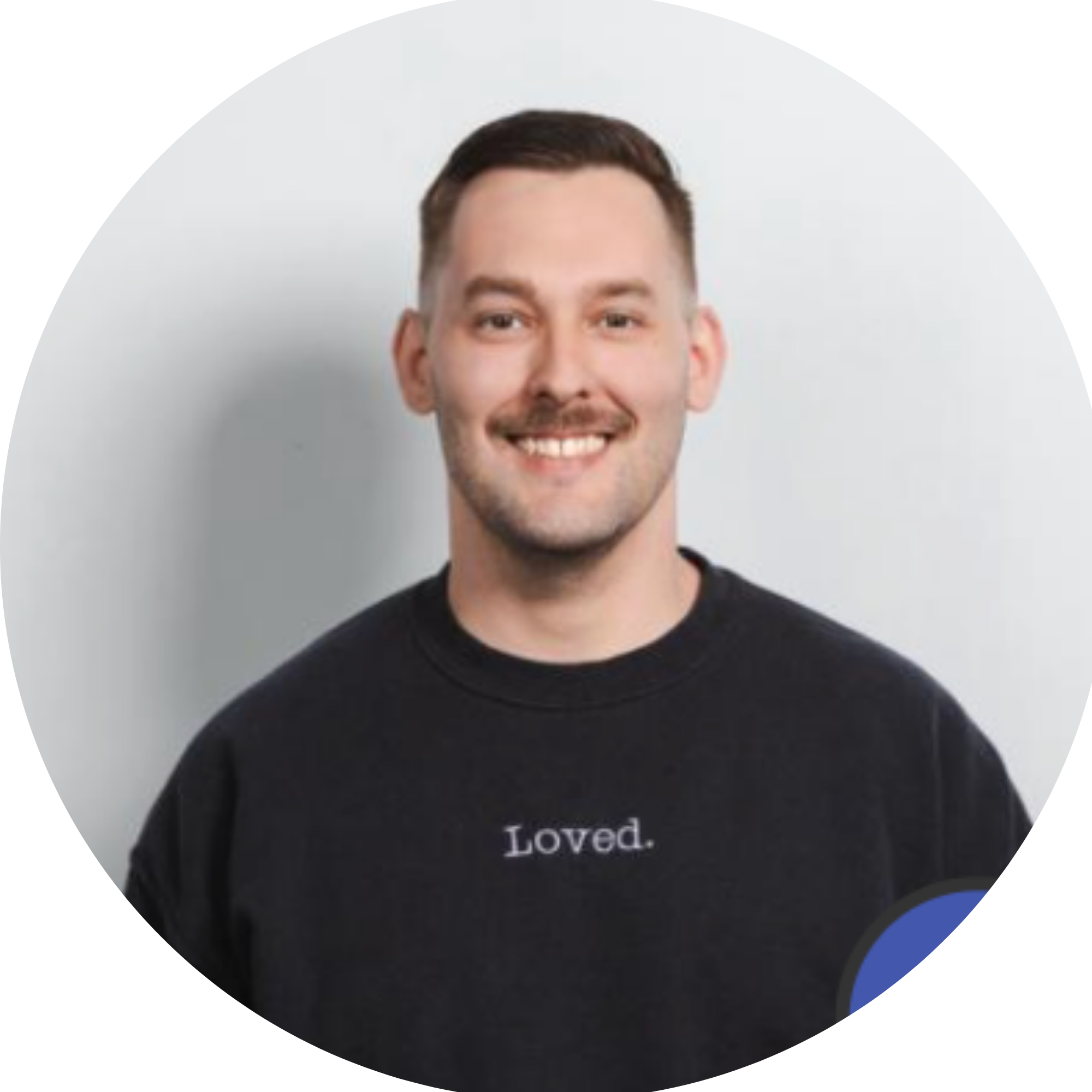 A woman with long wavy hair wearing glasses, smiling, in a setting with wooden cabinets and a light-colored wall.