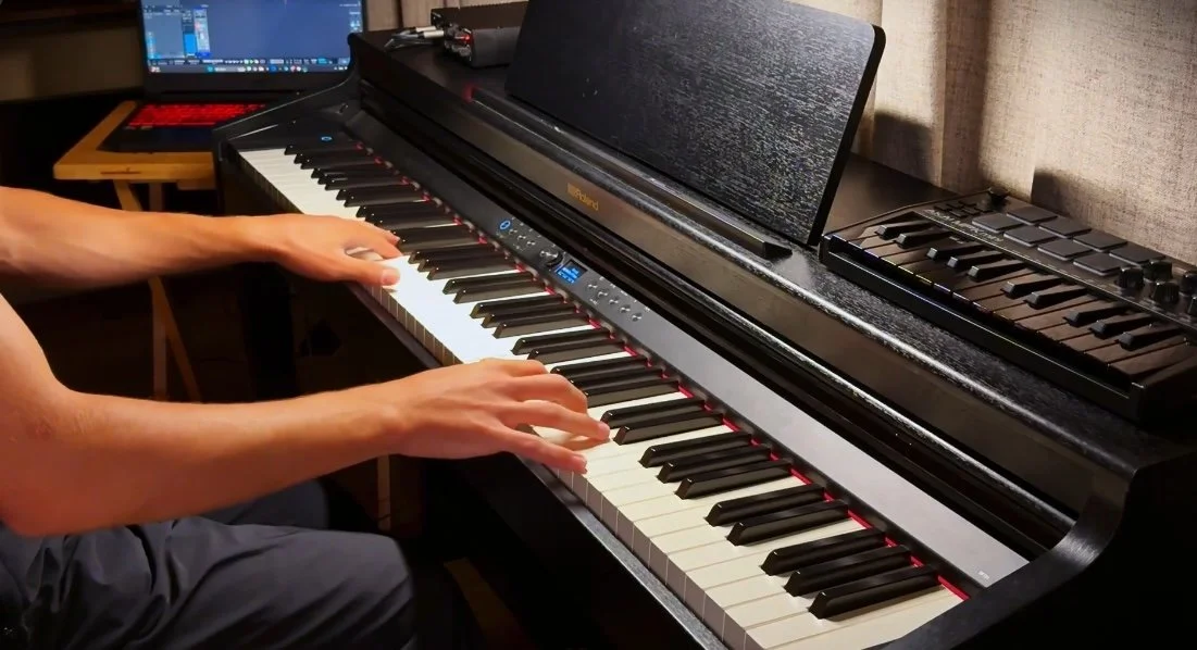 Person playing a digital piano with a computer monitor in the background.