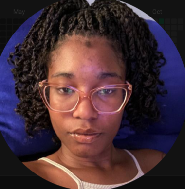 A woman with curly hair wearing glasses and a white tank top, lying on a blue pillow.