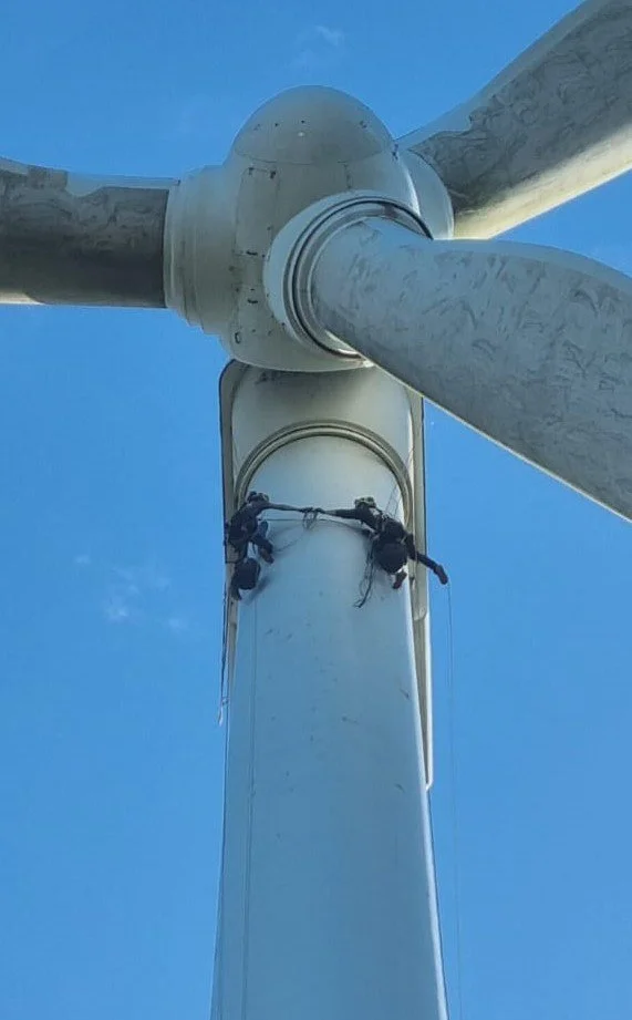 Two workers performing maintenance on a wind turbine under a clear blue sky.
