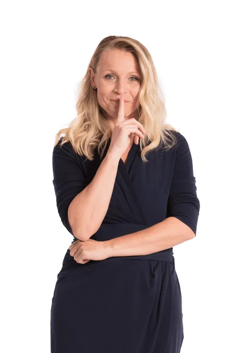 Woman with finger on lips, signaling "shush" gesture, wearing a black dress against white background.