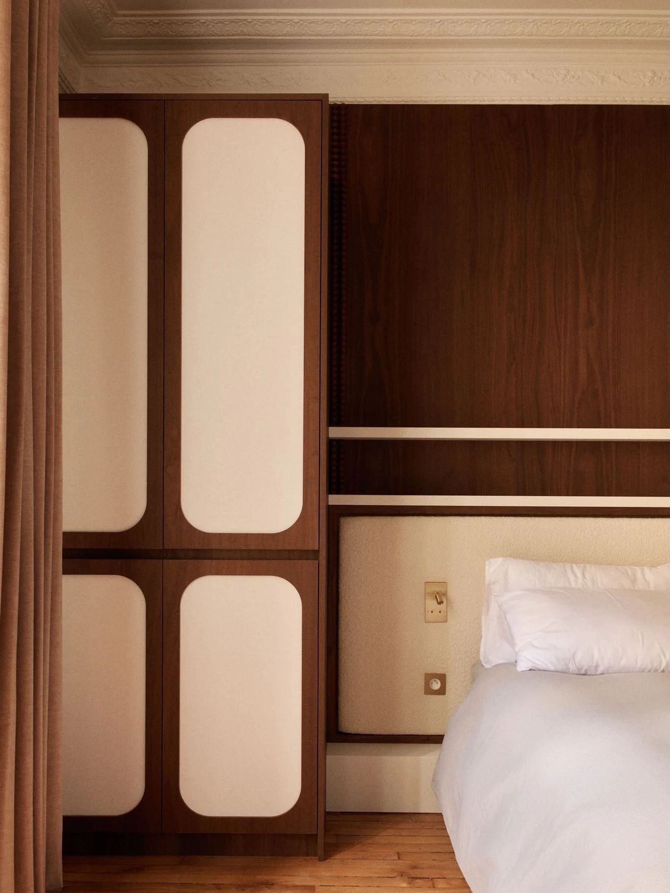 Dans la chambre principale du projet Bourdonnais, le bois fonc&eacute; cr&eacute;e un contraste fort et structurant. Le d&eacute;tail de l&rsquo;encadrement souligne les lignes du lit et donne du rythme &agrave; la pi&egrave;ce, tout en s&rsquo;int&e