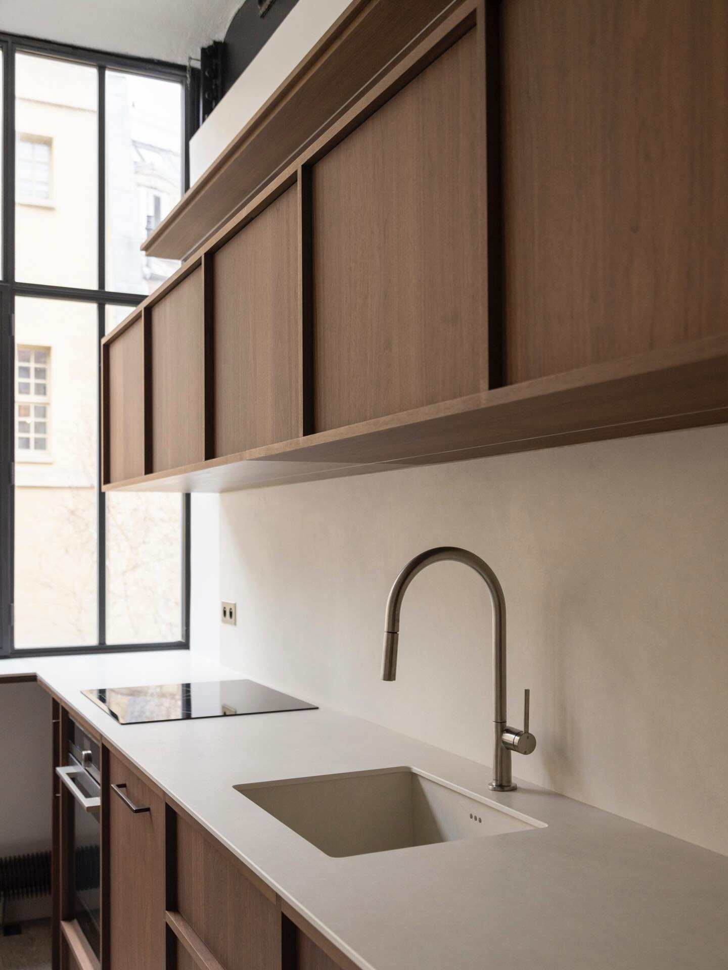 Dans cette cuisine du projet Turenne, les fa&ccedil;ades en noyer massif courent du sol au plafond et structurent l&rsquo;espace. Plan de travail en pierre, robinetterie int&eacute;gr&eacute;e, &eacute;lectrom&eacute;nager encastr&eacute; : l&rsquo;e