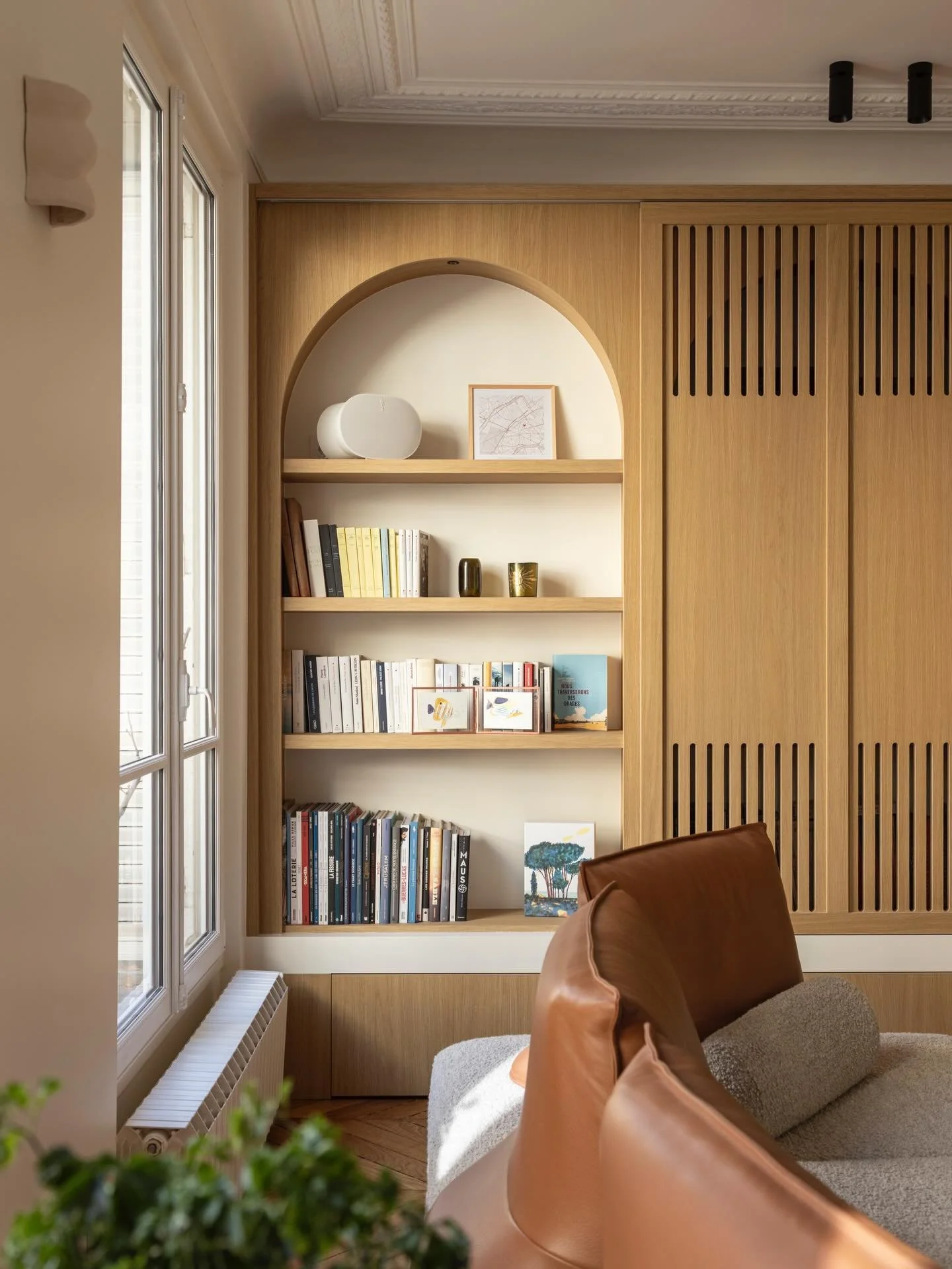 Dans ce salon du projet L&eacute;on Cognet, la biblioth&egrave;que sur-mesure en ch&ecirc;ne int&egrave;gre une niche en arcade et des portes coulissantes &agrave; lames verticales. L&rsquo;ensemble a &eacute;t&eacute; r&eacute;alis&eacute; par Aurel