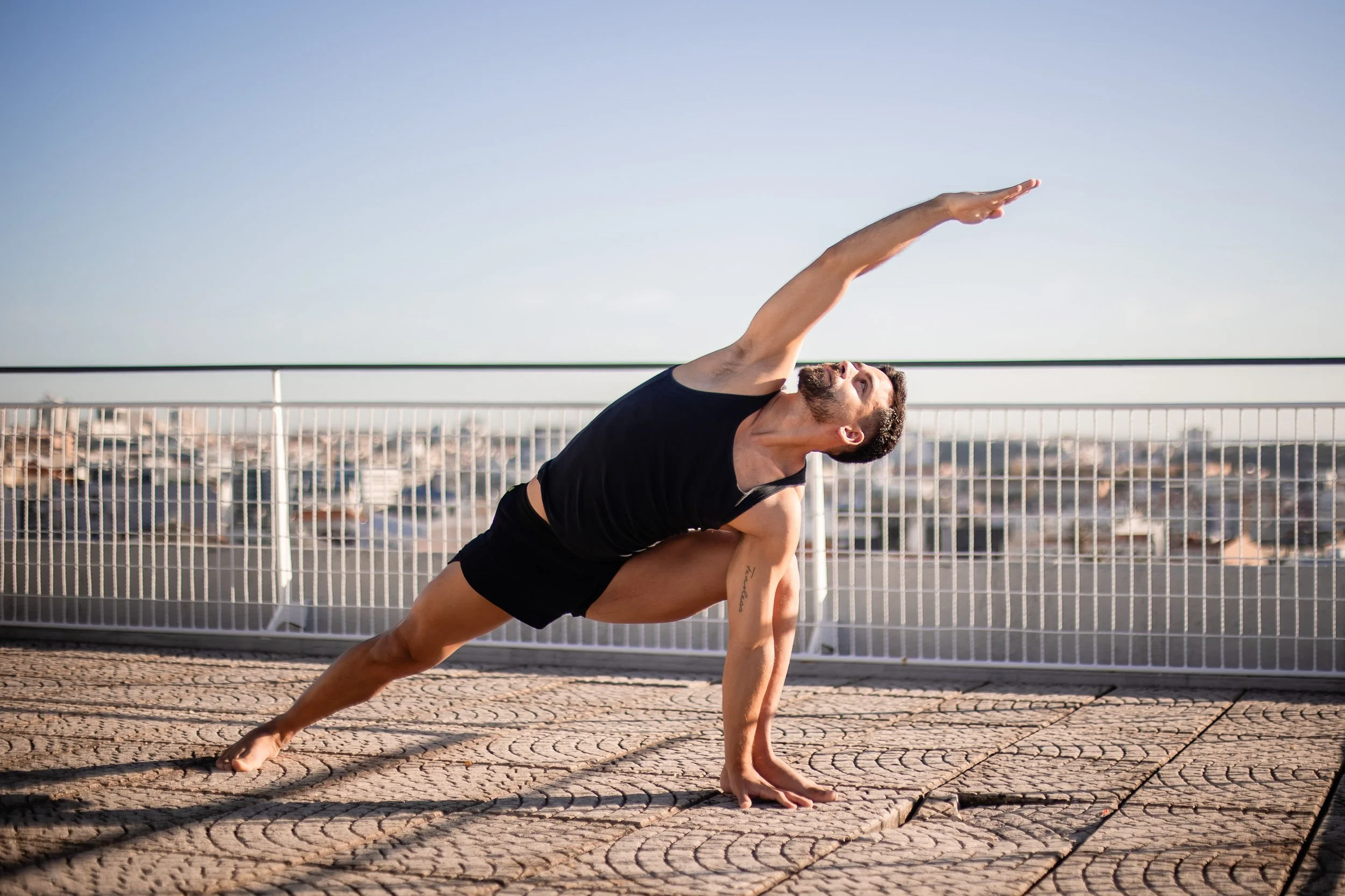 Man doing a yoga pose on a rooftop terrace with city skyline background