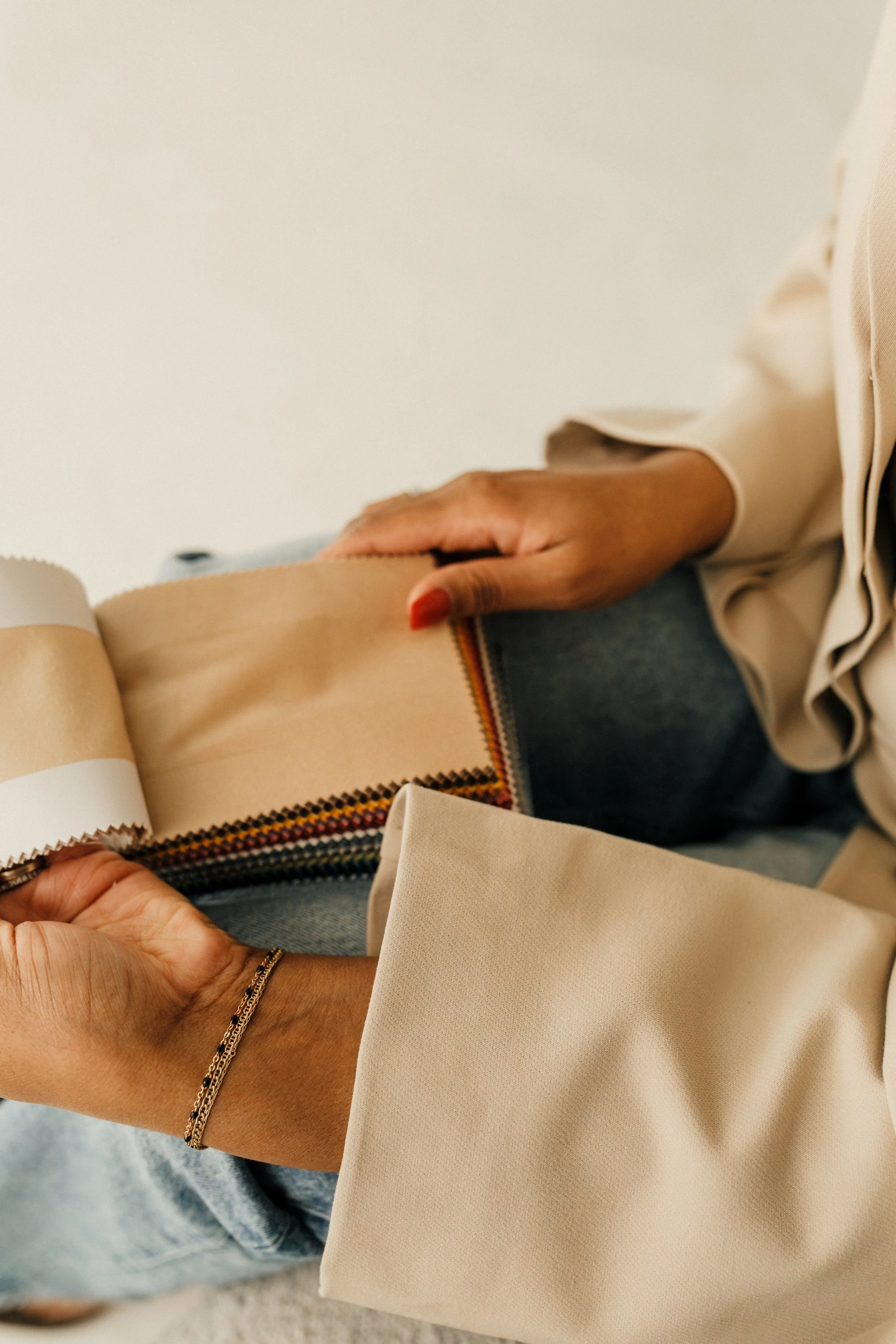 Person holding fabric sample swatch with beige and rainbow-colored stripes.
