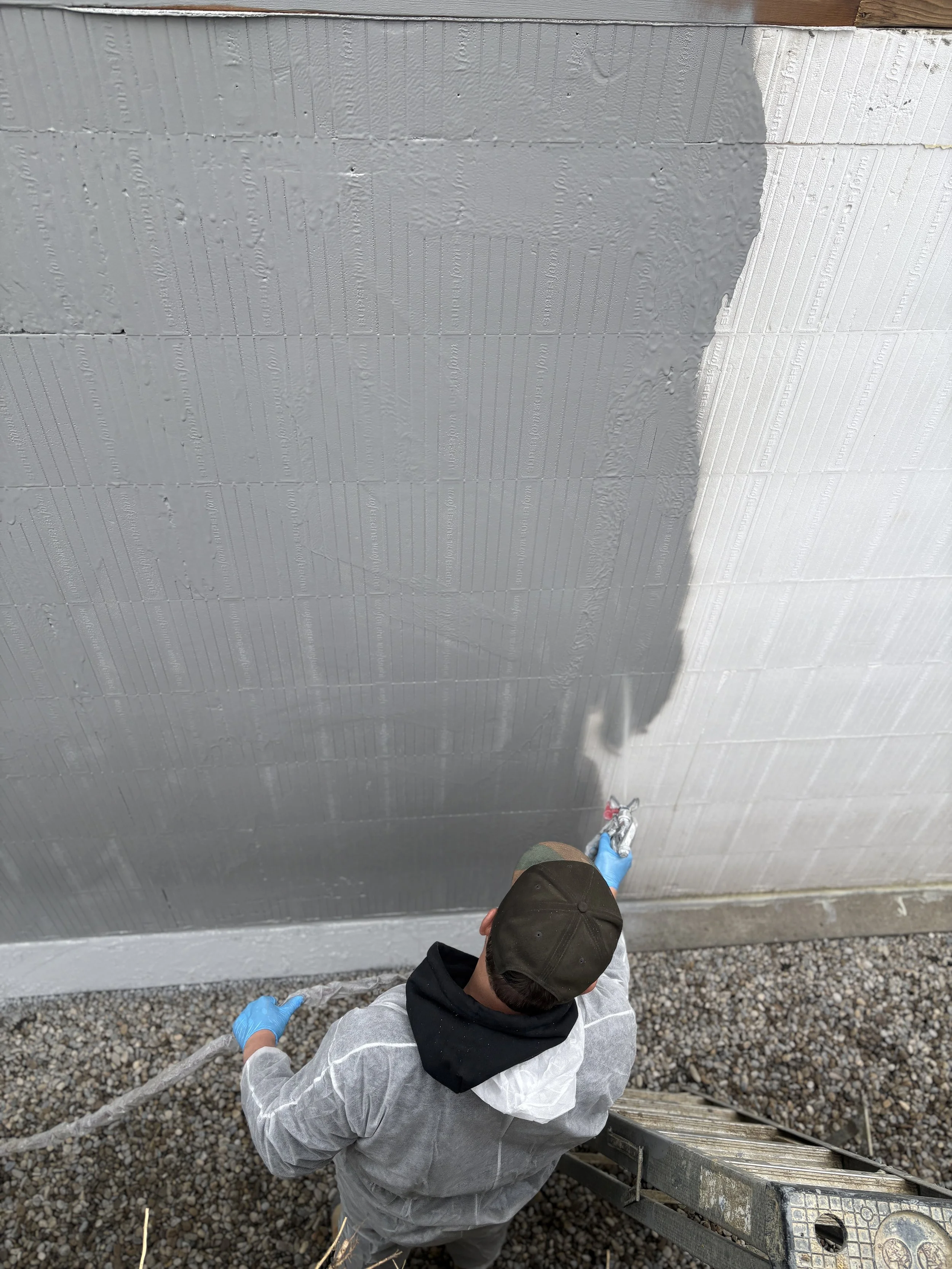 man applying composite waterproofing to a foundation of new construction home
