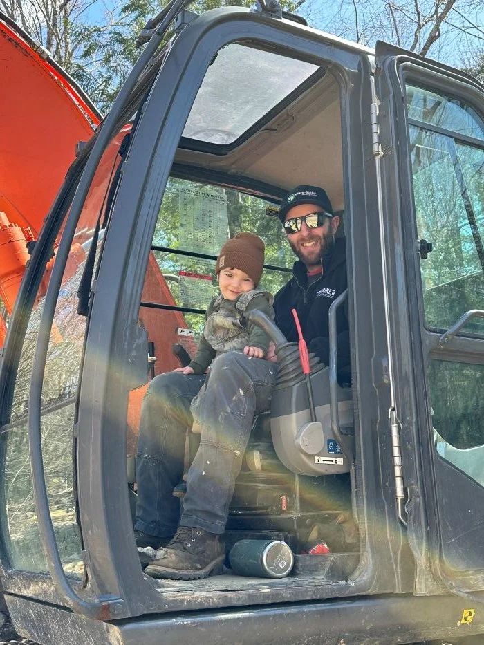 excavator operator with his son installing a septic system in an orange escavator