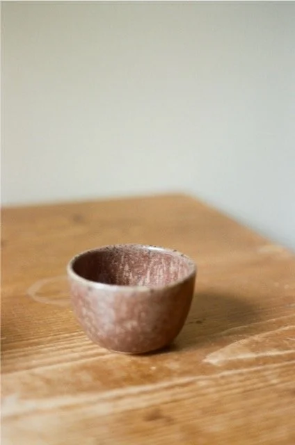 A small, rough-textured ceramic bowl on a wooden surface with a plain, light-colored wall in the background.