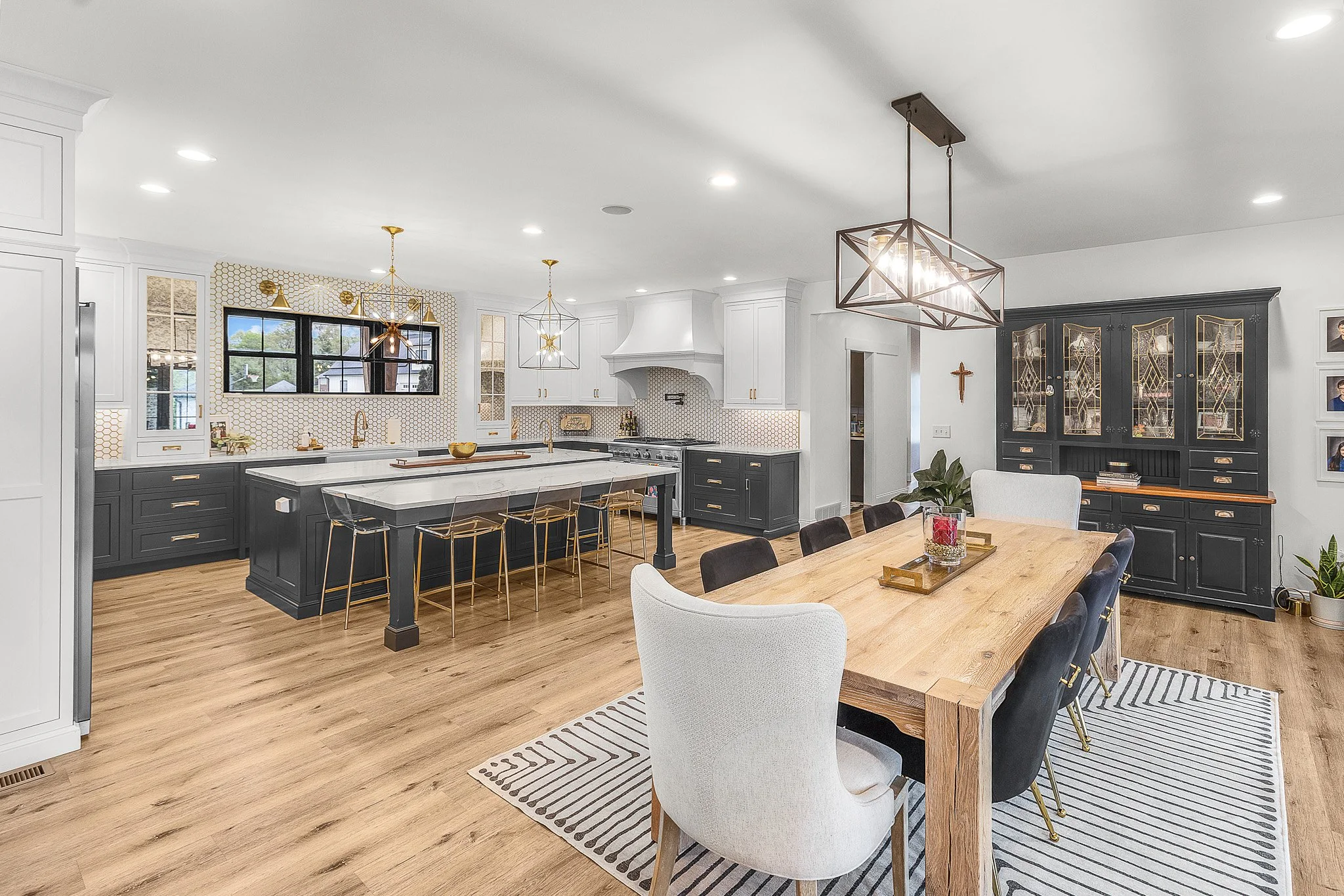 Modern kitchen with white cabinets, a large island with seating, floral wallpaper, and dual bubble chandeliers.