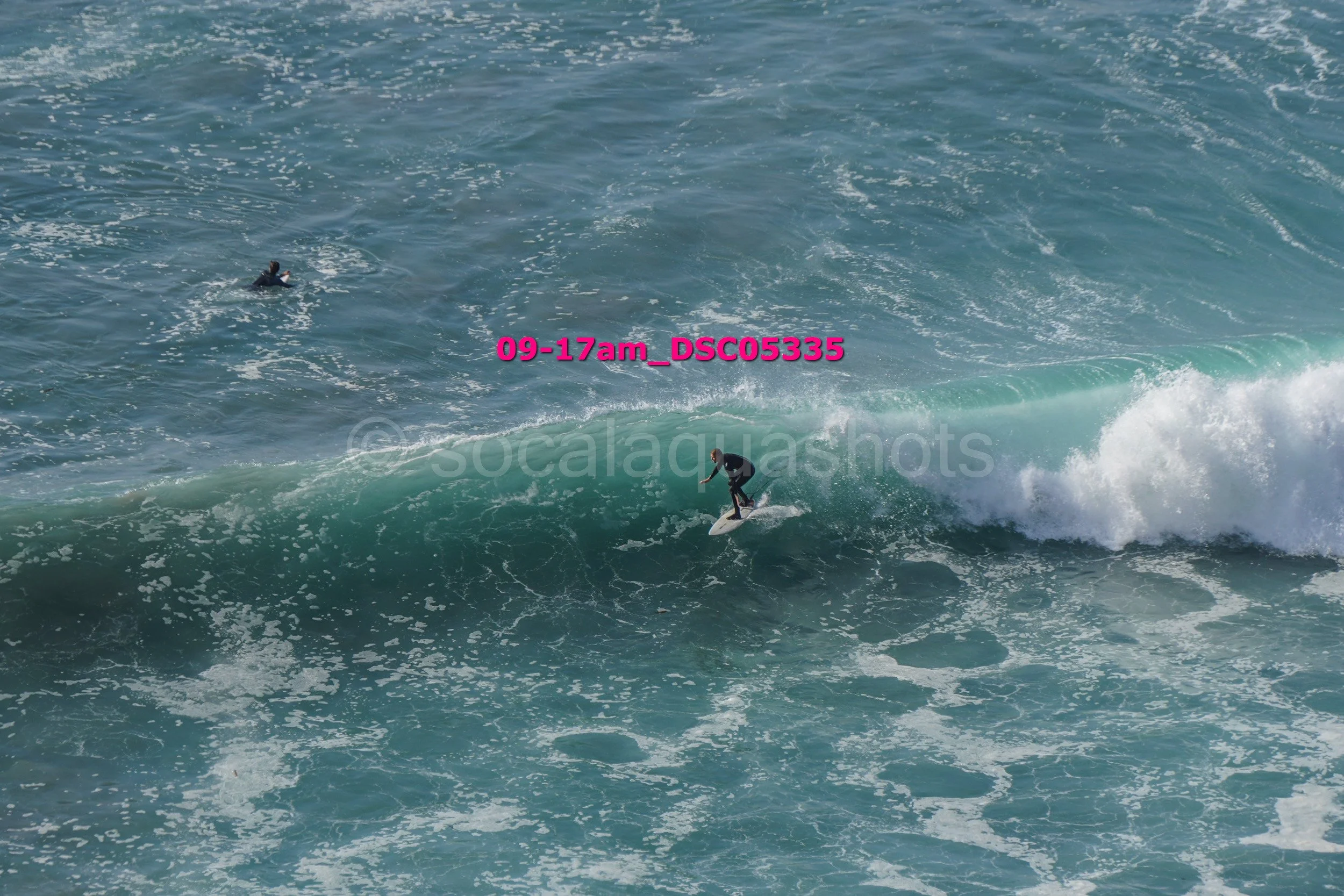 A surfer riding a wave in the ocean with another person swimming nearby.