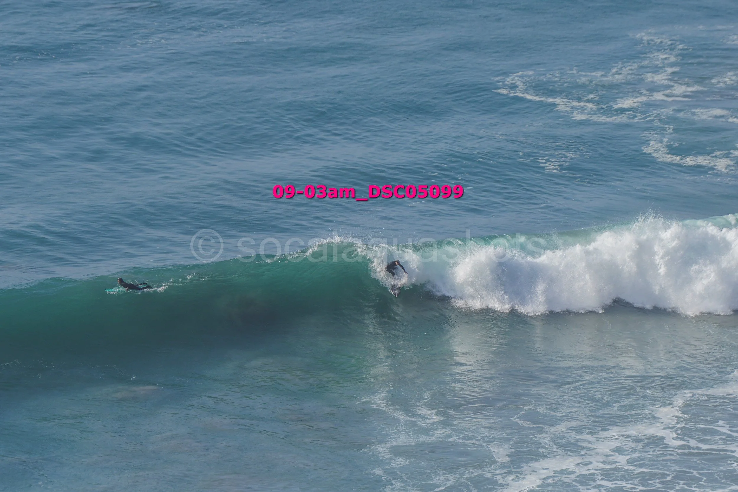 Two surfers riding and paddling on ocean waves on clear day