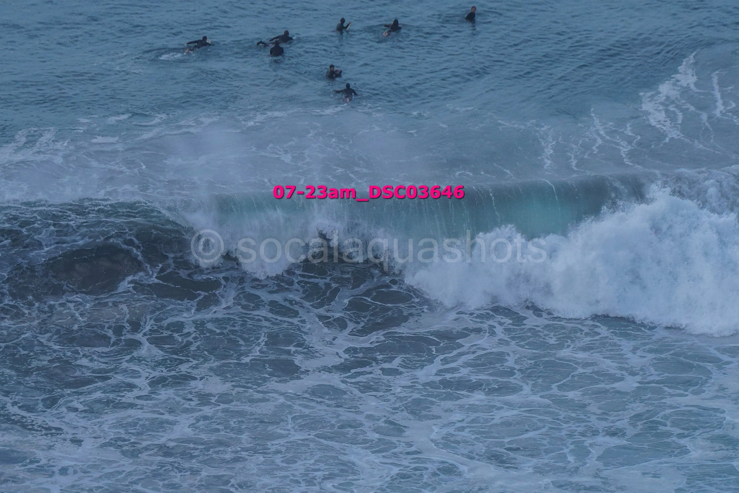 A group of surfers waiting on the ocean to catch a wave, with one surfer riding a wave closer to the shore.