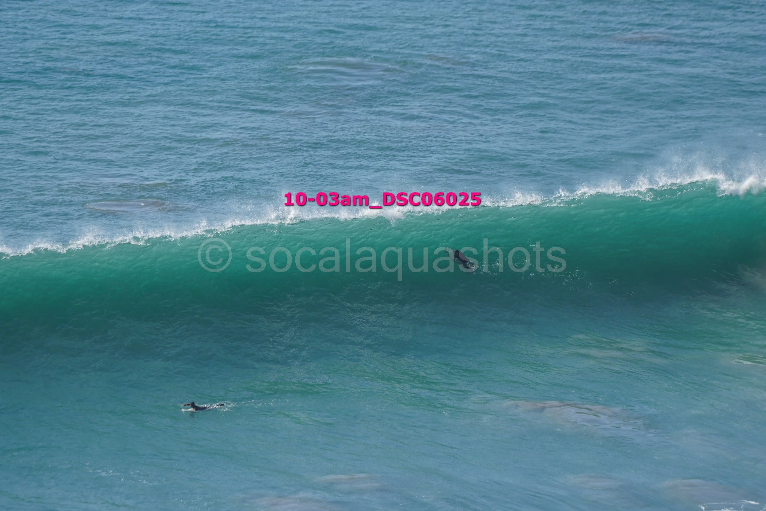 A person surfing on a large wave in the ocean with another surfer swimming nearby.