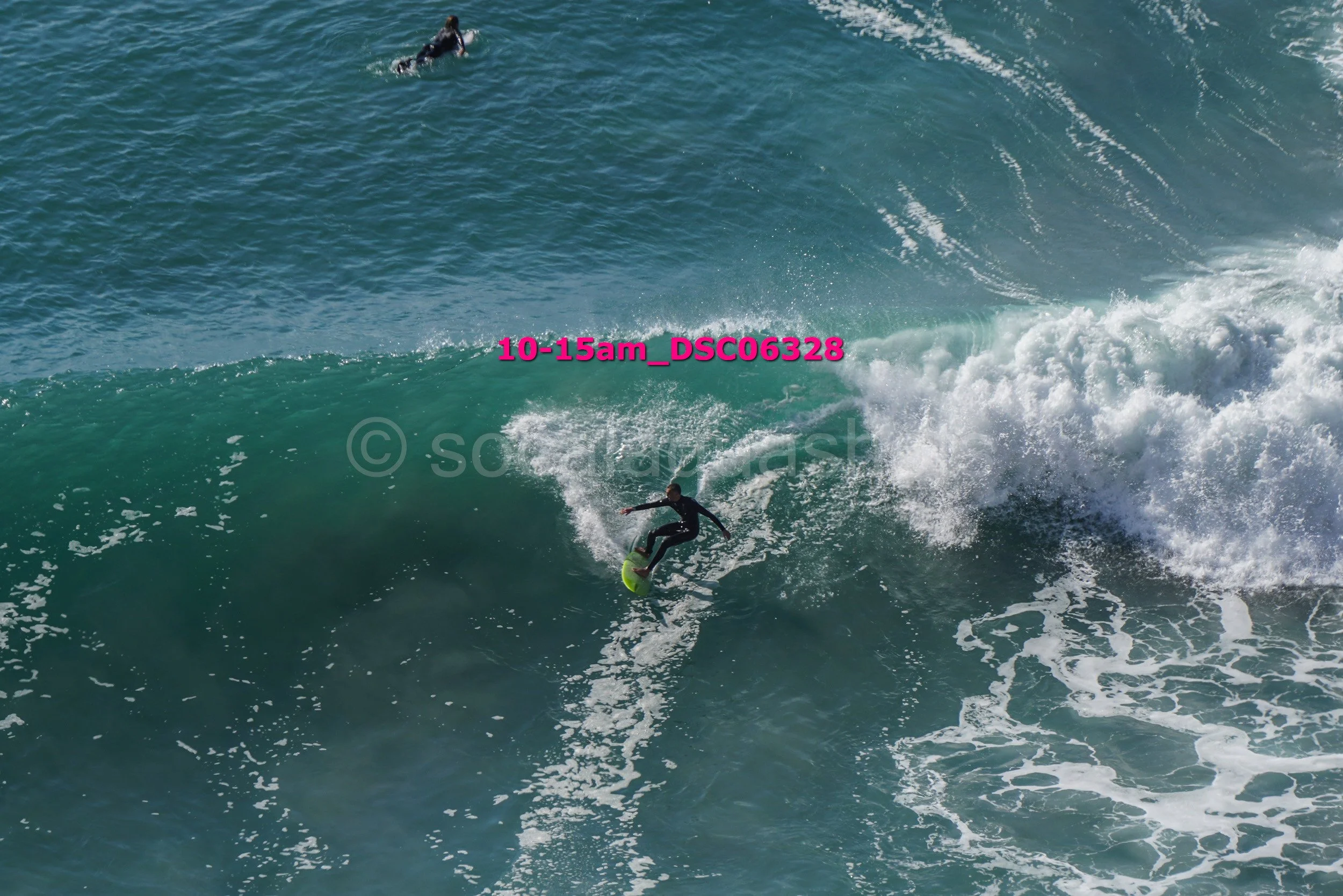 A person surfing a large wave with another surfer visible in the background.