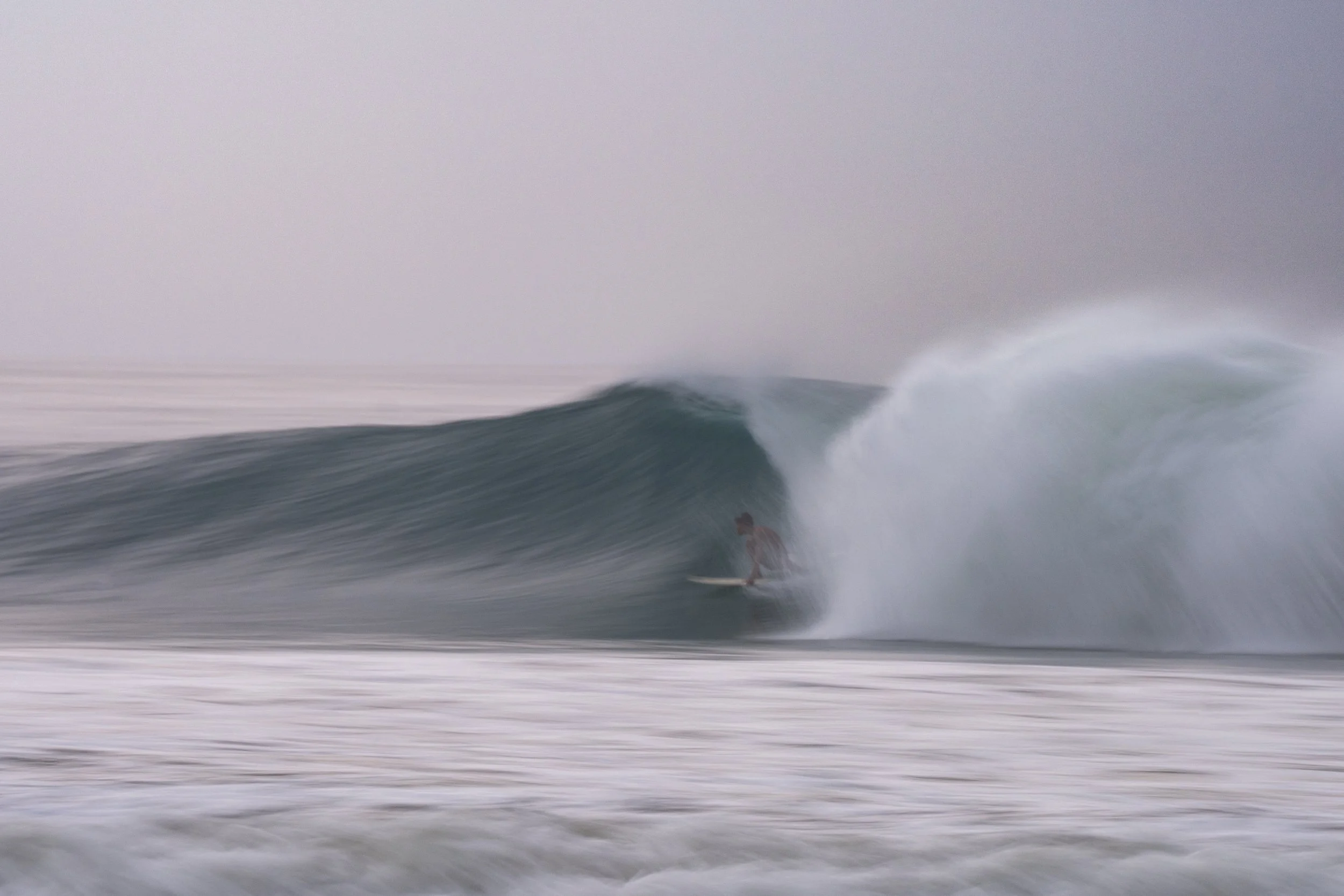 A person surfing on a wave in the ocean, with the wave curling over and water spray.