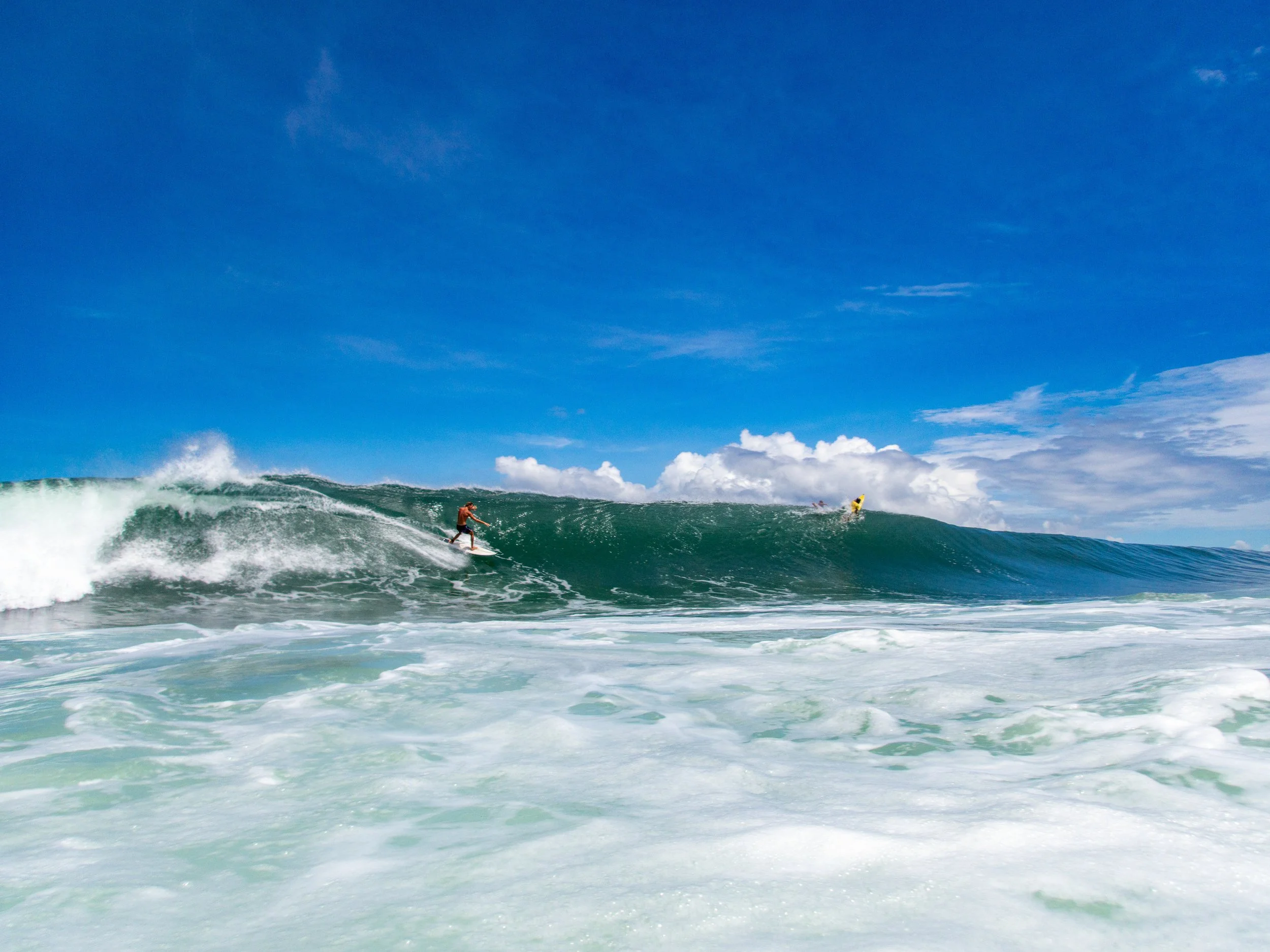 Surfer riding a large wave in the ocean with clear blue skies.